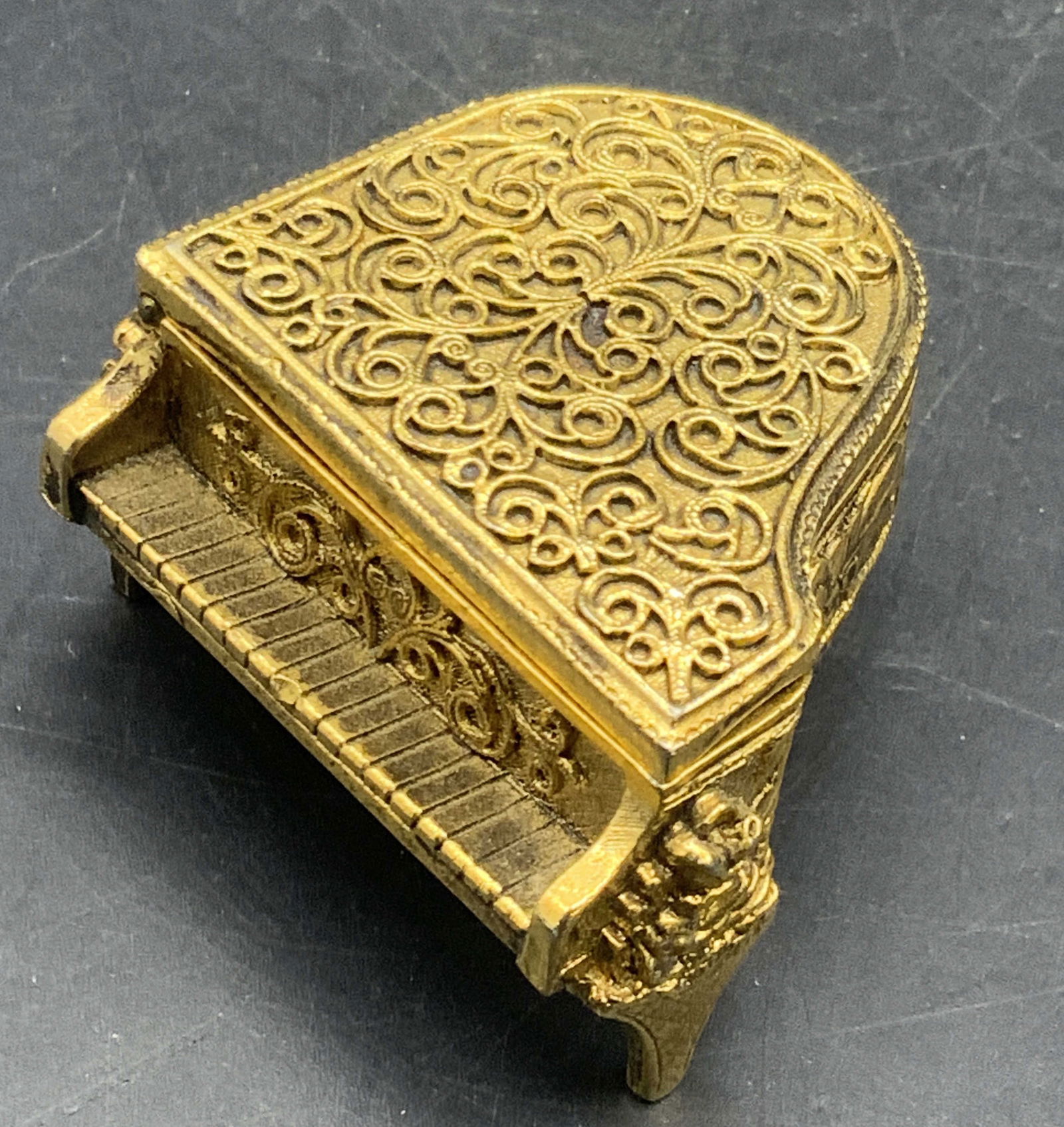 Vintage AVON Baby Grand Piano Solid Perfume Holder: A vintage gold tone metal baby grand piano solid perfume holder. Raised scrollwork to the design. Measures approx. 2W x 1H in. Interior marked AVON. Interior has an area where the solid perfume would