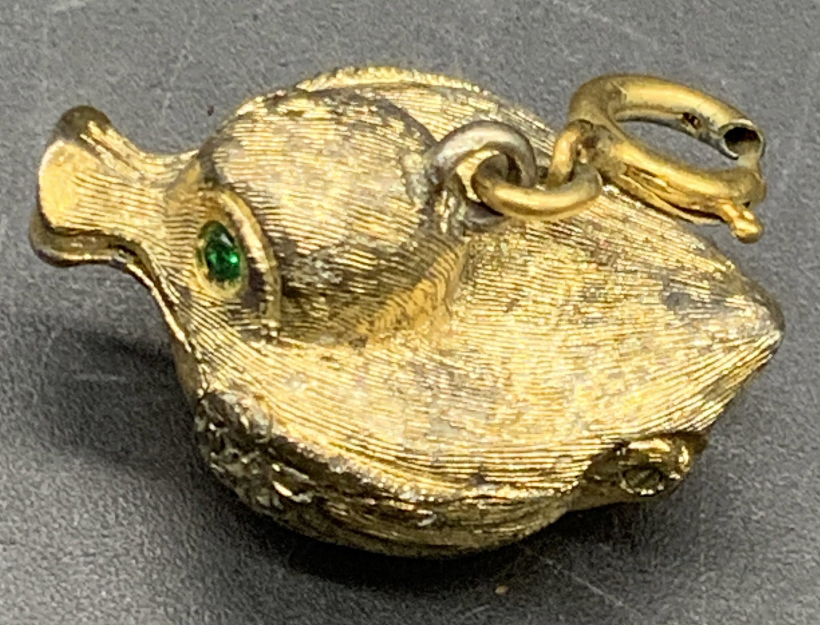 Vintage Crystal Eyed Duck Locket Pendant: A vintage gold tone metal duck figural locket pendant. Green faceted crystal eyes to the piece. C Spring closure attached to the bail. Measures approx. .5H x 1W in. Measured at widest point. Opens wit