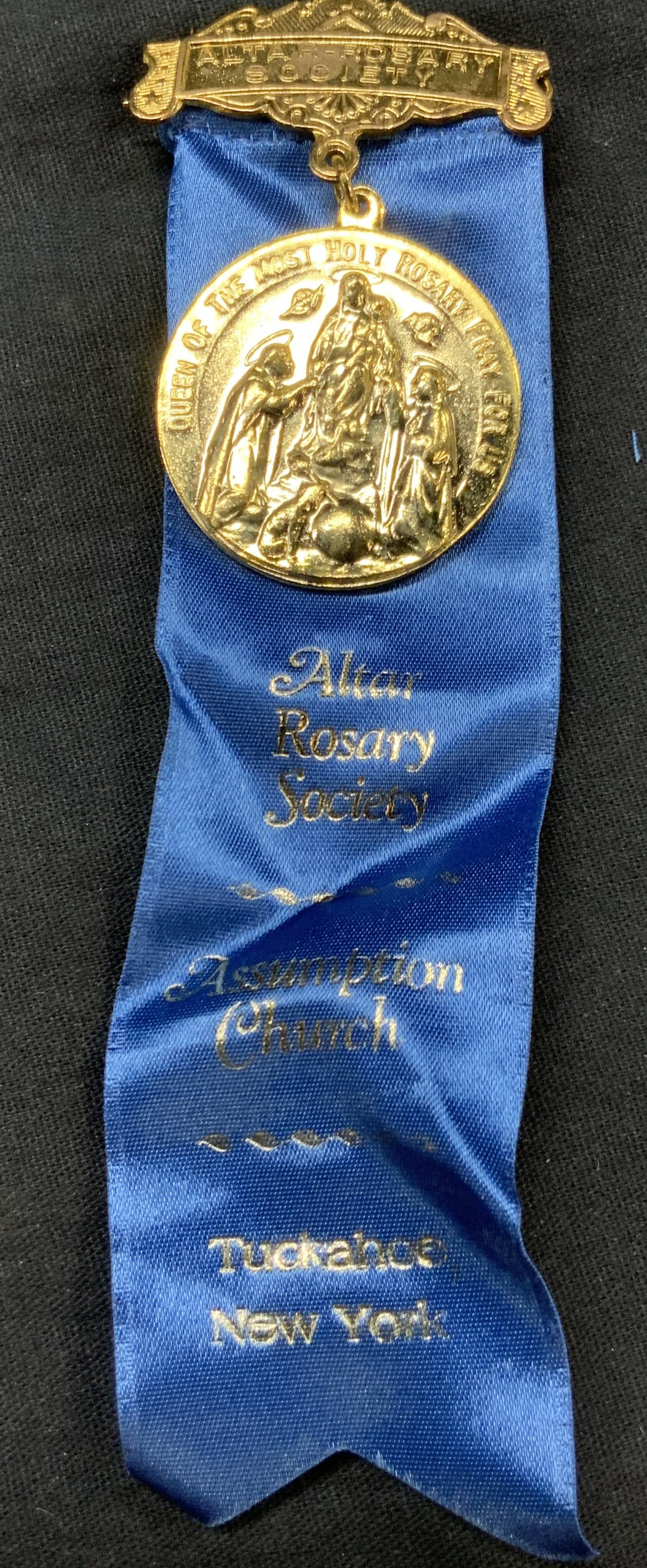 Gilt Metal Altar Rosary Society Ribbon: Gilt metal and blue ribbon reading Altar Rosary society, assumption church, adorn with a medallion with a raised image of Mary holding the Christ child. Approx 6 x 1.5 inches. Minor wearing to gilt an