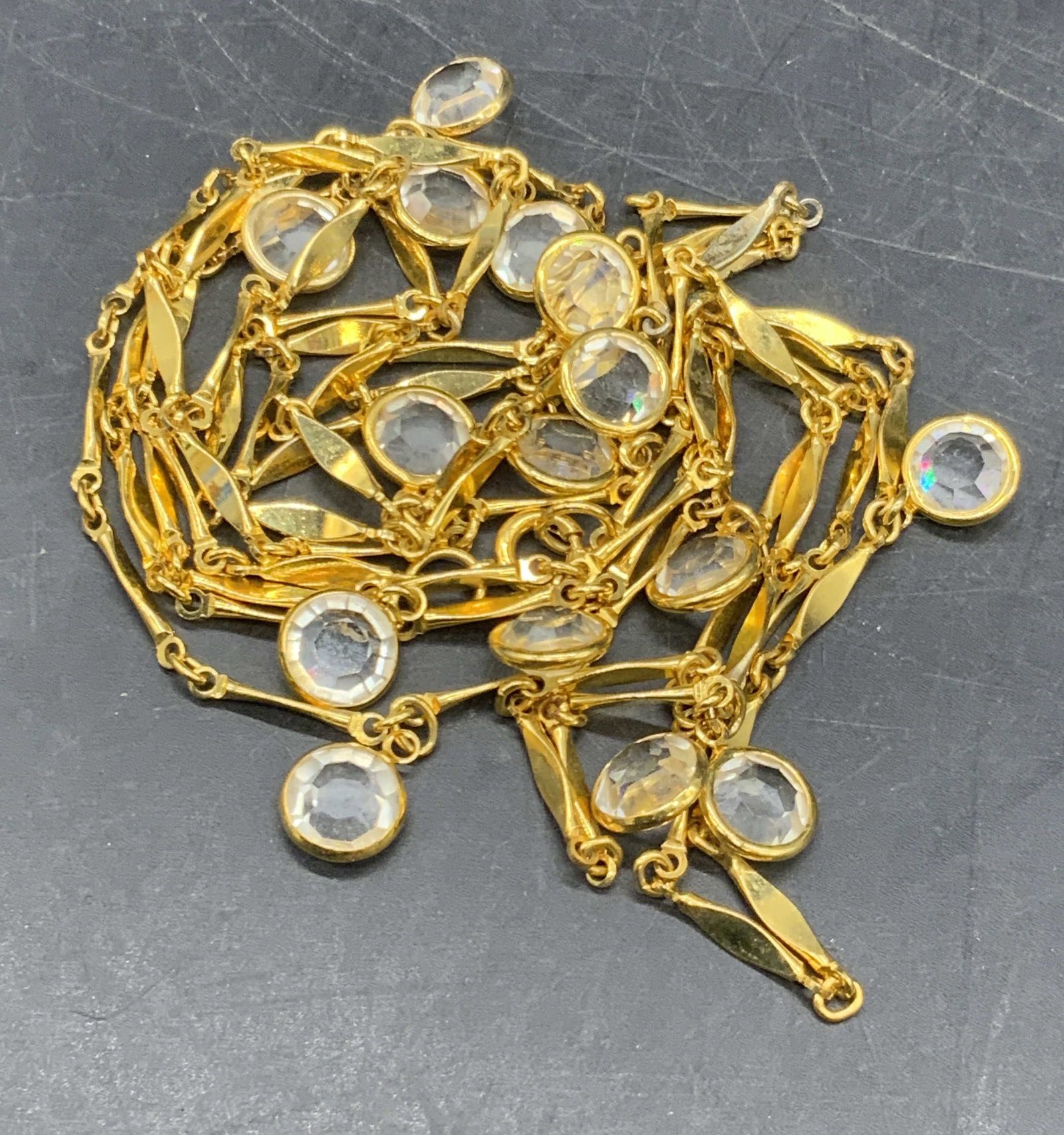 Gold Tone Metal Dangling Crystal Necklace: A gold tone metal necklace featuring dangling faceted colorless crystals. Measures approx. 50 inches from end to end. Secures with C Spring clasp closure. Some surface wear consistent with age and use