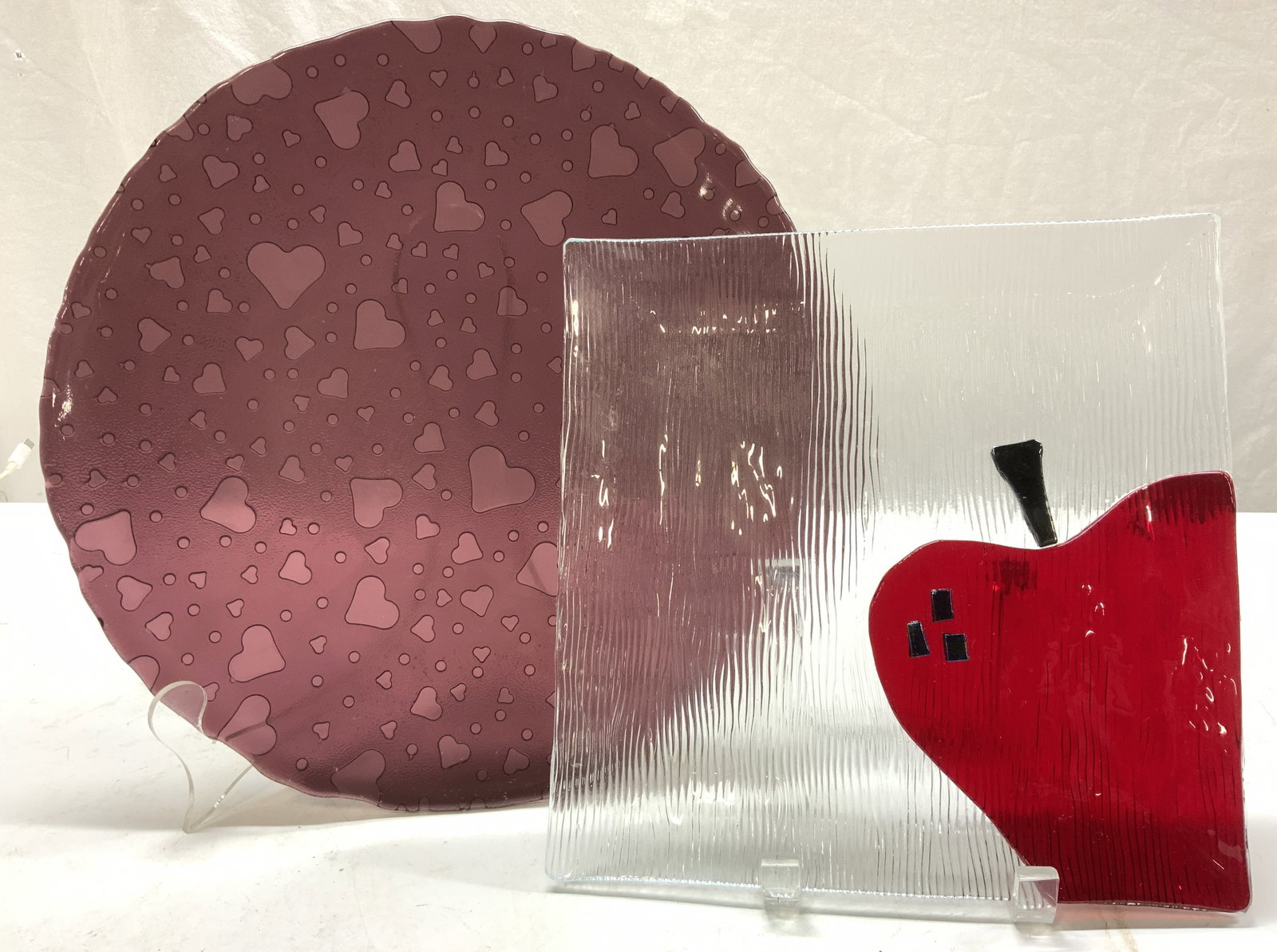 Lot 3 Art Glass Trays, Apple & Heart Motif: Square art glass tray with red corner apple, ribbed underside. Measures 9.25 in. Sq Round amethyst toned glass tray with embossed heart pattern on the underside, measures 12.5 in. Tableware, Trays, Gl