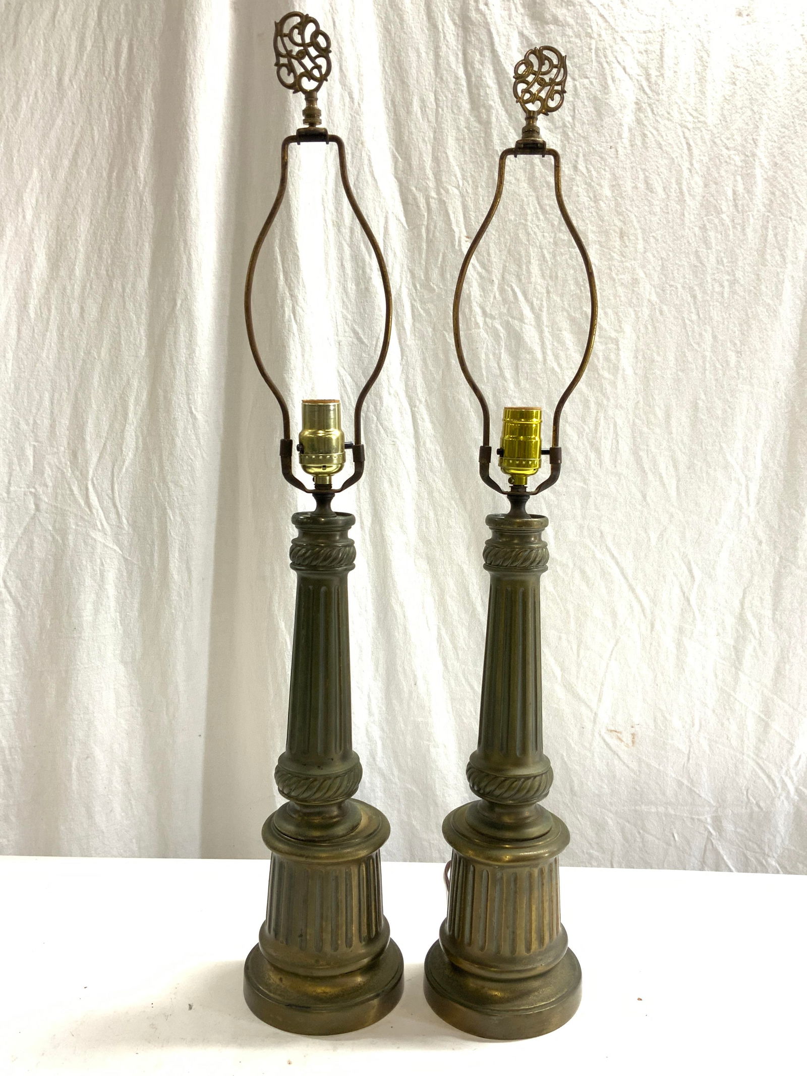 Pair Vntg Gilt Metal Pillar Table Lamps: Lot includes 2 lamps. Each are gilt metal, possibly brass. Lamps each have pillar forms. Lamps each includes harps and finials. Lamps each measure approximately 31 inches tall 5.25 inches wide. Lamps,