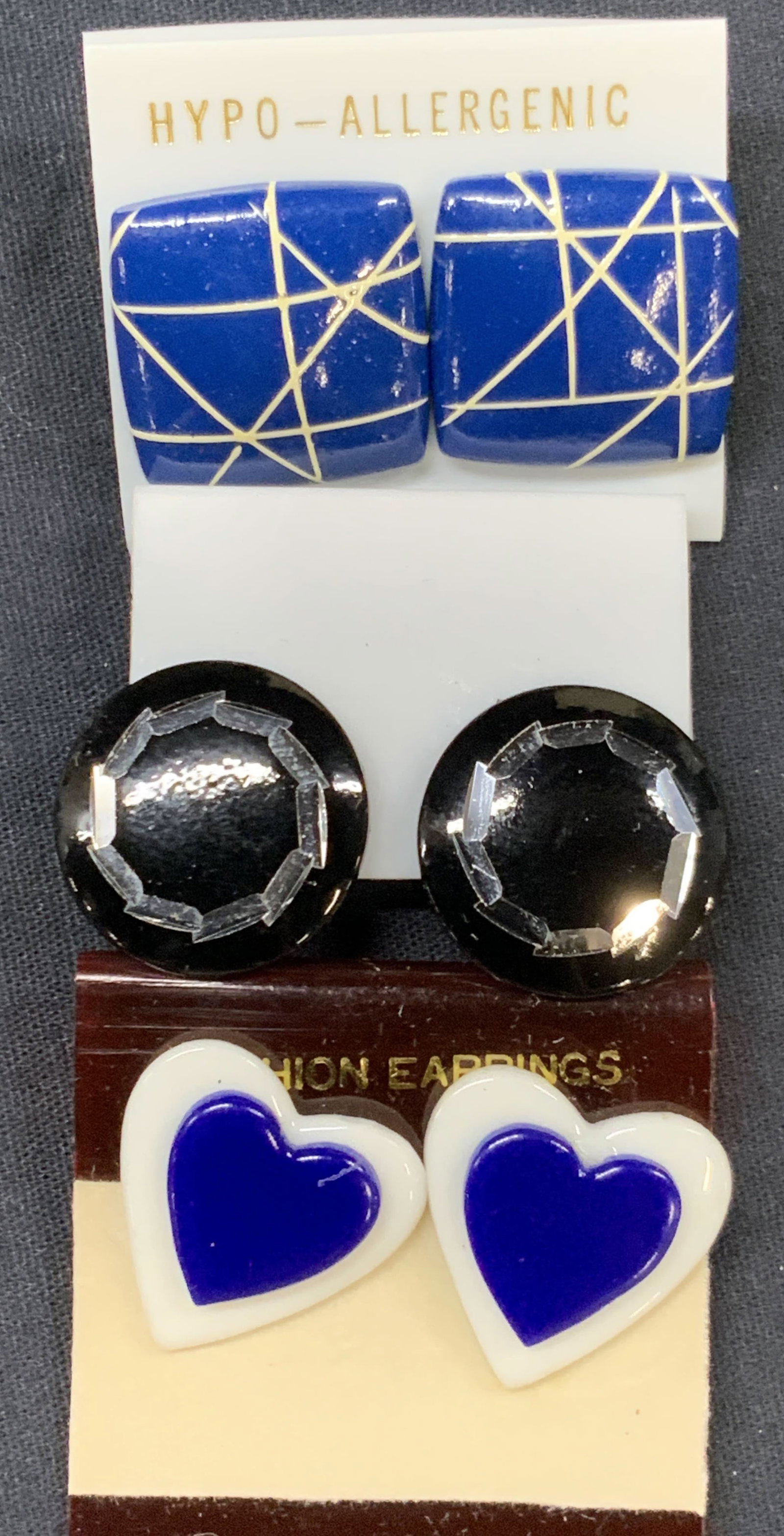 Lot 3 Wooden & Acrylic Earrings: Lot of 3 stud earrings, 1 black acrylic circular clip on earrings and 1 heart shape blue and white acrylic earrings and 1 blue wooden earrings. Approx 1 x 1 inches. Minor surface wearing to earrings E