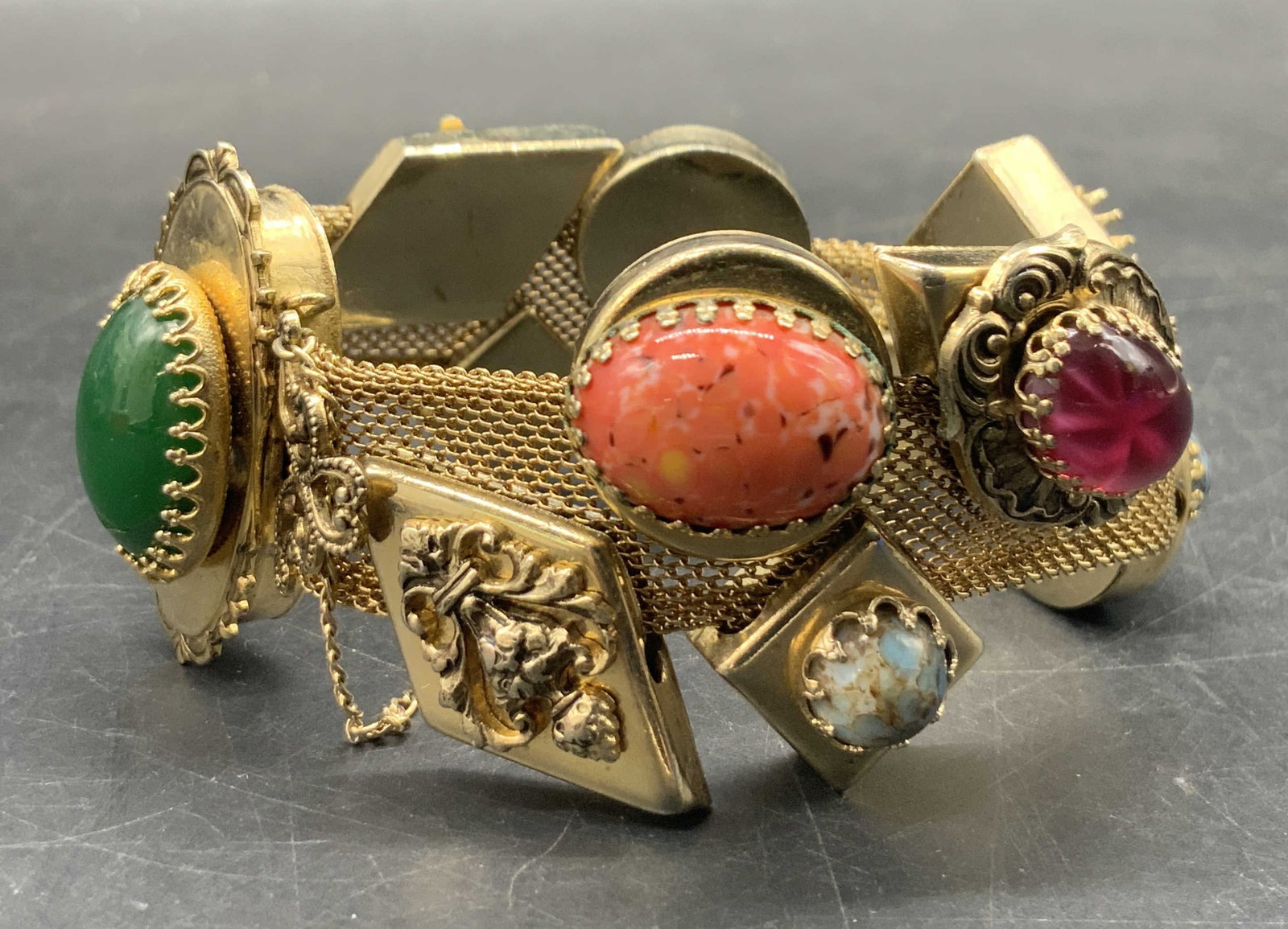 Vintage Costume Cabochon Mesh Bracelet: A vintage gold tone metal mesh bracelet featuring multicolored prong set costume cabochons. Other adornments feature crest motifs. Safety chain towards clasp. Bracelet diameter measures approx. 2.5 in
