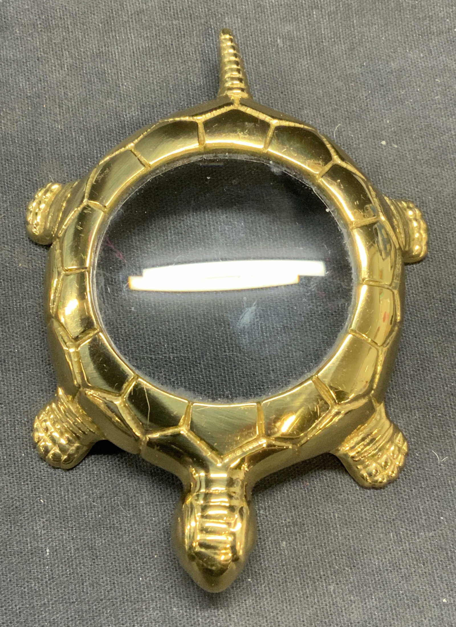 Gold Tone Turtle Motif Magnifying Glass: Gold tone table top ,gamifying glass with turtle motif. Embossed raised surface. Measures approx. 4.25 x 3 x .75 inches. Some scratching observed. Turtle magnifying glass, magnifying glass, gold tone 
