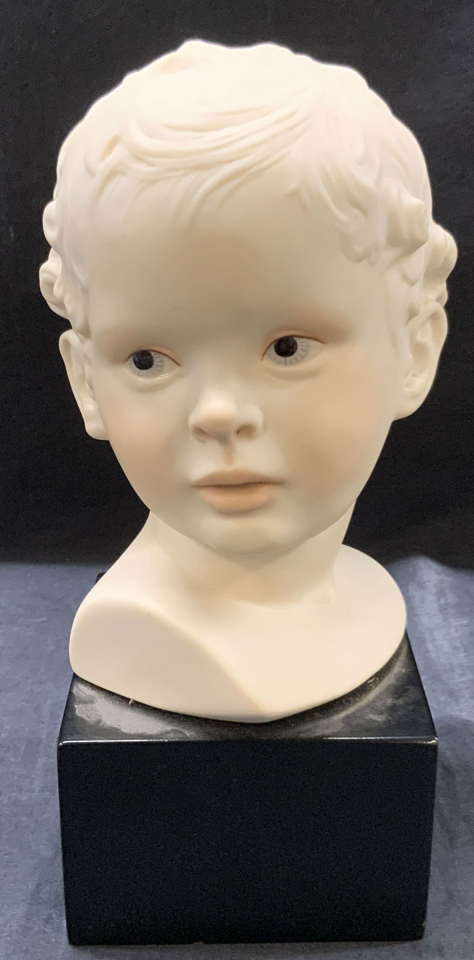 Cybis Sgd Porcelain Eros Bust: Signed, Cybis white porcelain bust of Eros affixed to a black wooden base. Hand painted eyes and blush to cheeks. Approx 10 inches tall, with base at 4 x 4 inches. Moderate surface wearing and wearing