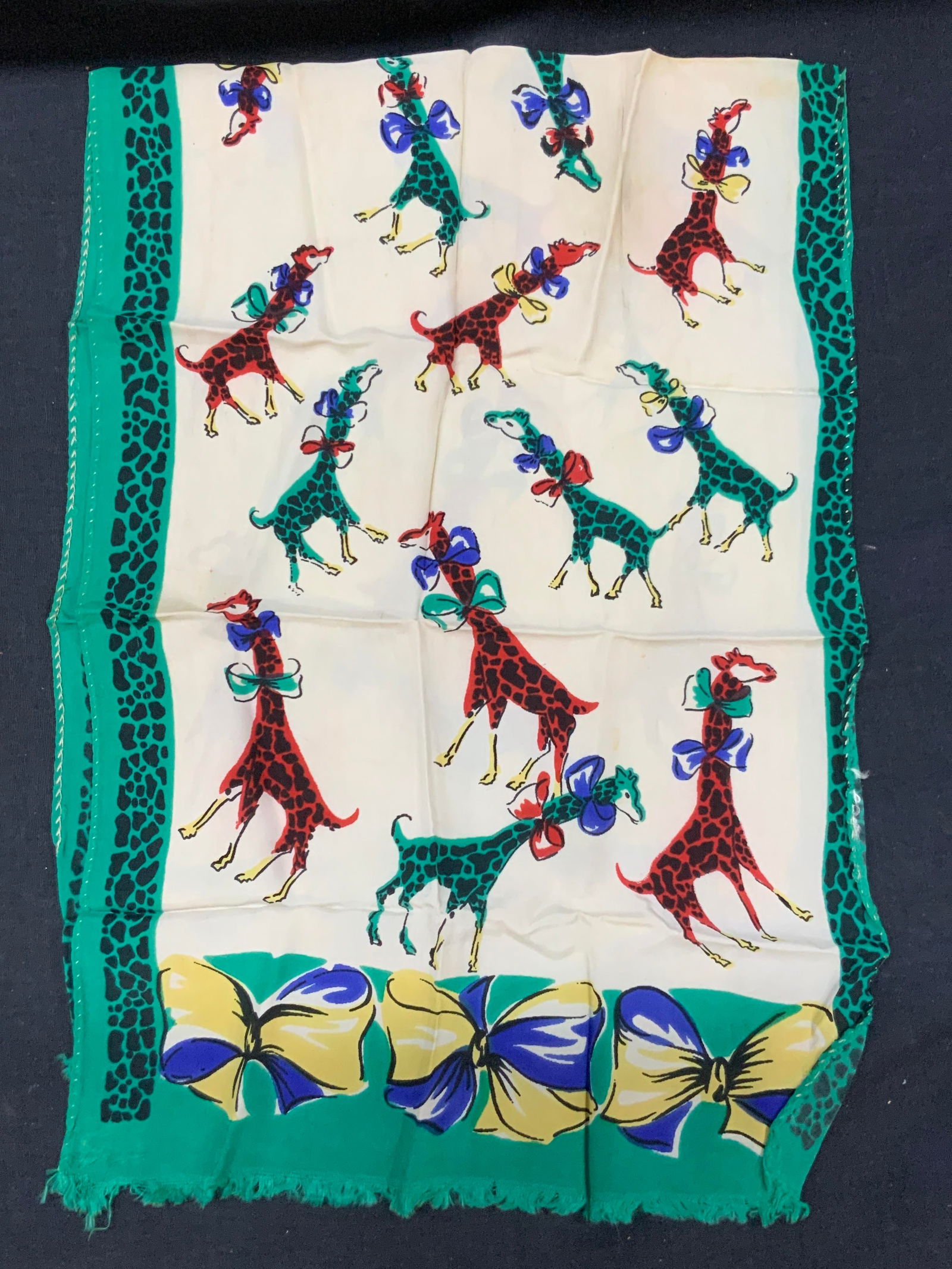 Vntg Giraffe Silk Child Scarf/ Textile: A vintage silk scarf with hand sewn edges with prints of red and green giraffes with giraffe prints on edges and blue and yellow ribbons On ends. Approx 31inches tall and 11 inches wide. Moderate disc