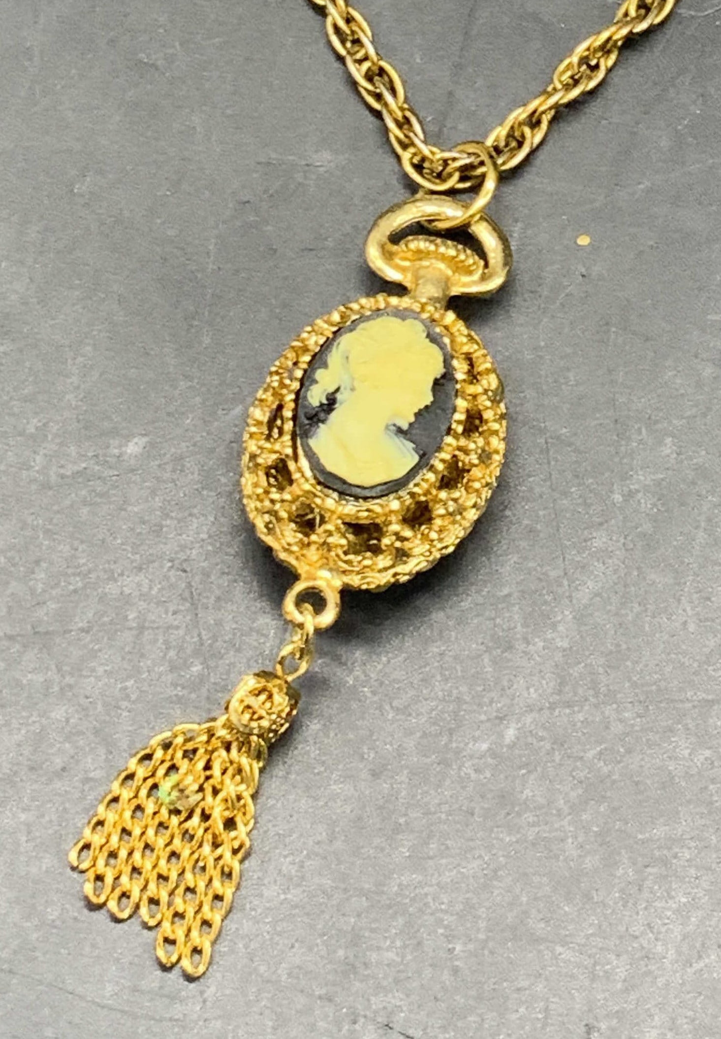 Vintage Cameo Pendant Necklace, Jewelry: A vintage gold tone metal necklace with a cameo pendant. The pendant features open gold tone metalwork backing and raised florals to the reverse. Cameo appears to be composite material. Necklace lengt