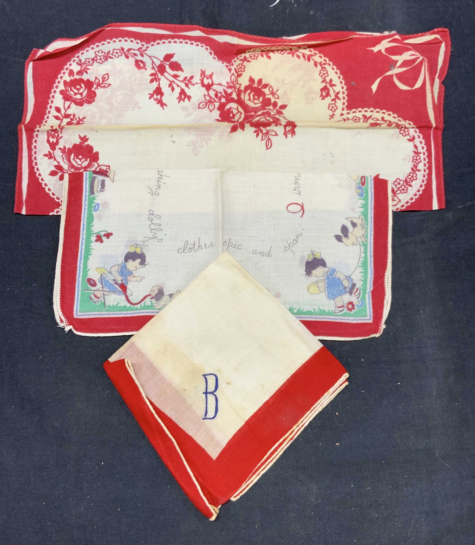 Lot 3 Vintage Red Tn Linens: Lot of 3 vintage red toned linens. 1 with red rose motifs and ribbons. 1 with red band and motifs of children with a nurse rhythm on it and 1 with a red band and blue B embroidered on the corners. Lar