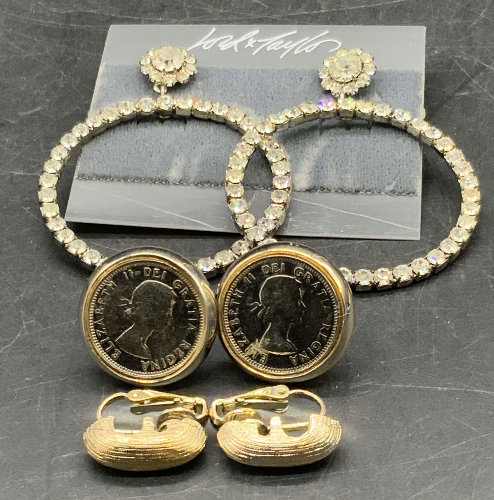 Lot 3 Vintage Metal Earrings, Lord & Taylor +: Vintage silver and gold tone metal earrings. Pieces have post or clip on backings. One pair of earrings features a currency motif which reads Elizabeth II Dei Gratia Regina. Another pair of earrings f