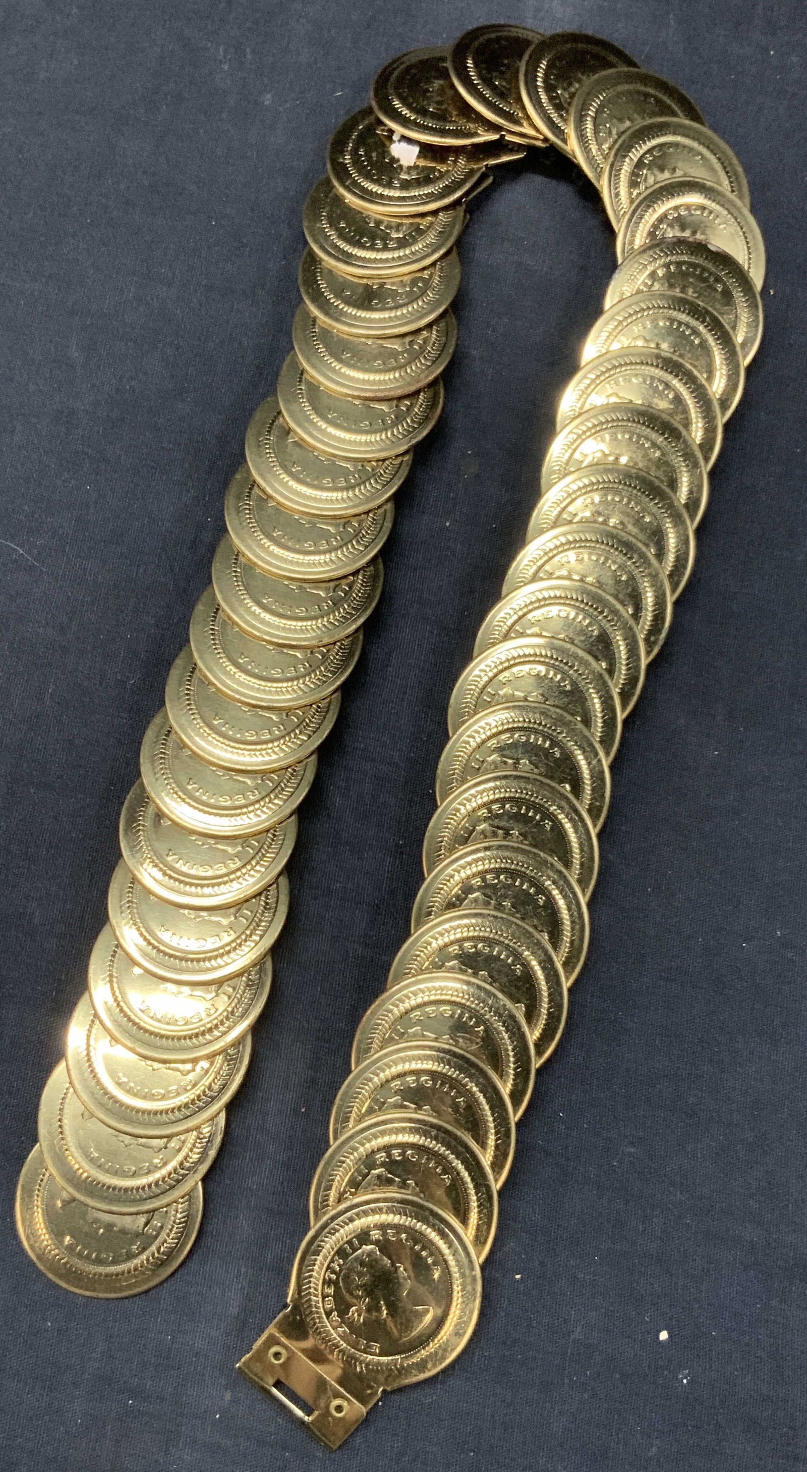 Queen Elizabeth Regina Gilt Metal Belt: Gilt metal crafted belt with elastic band. Embossed with Elizabeth Regina gold coin plates. Approx 10 inches across and 23 inches long. Moderate surface wearing to metal due to age and use. Vintage be