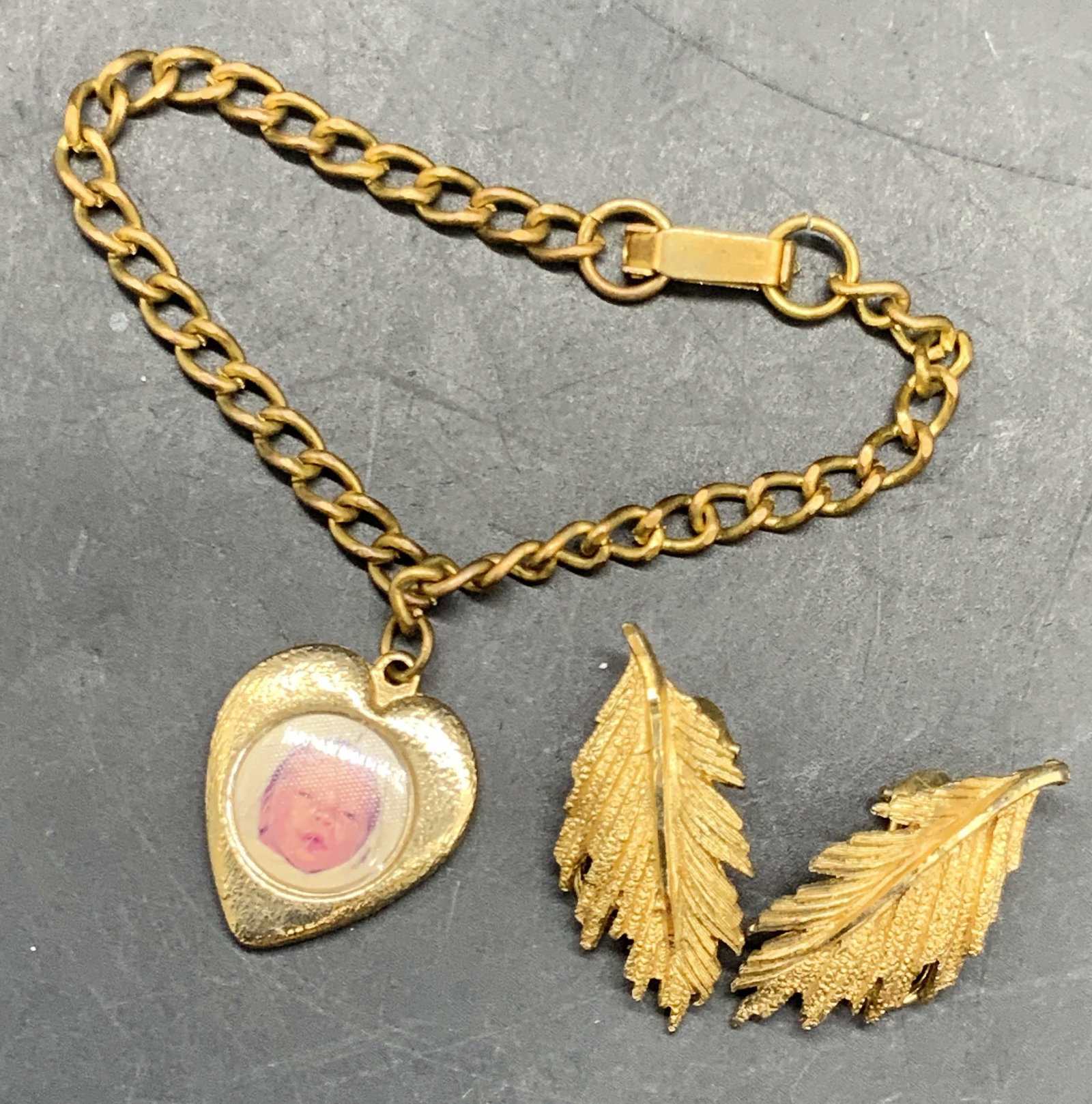 Lot 2 Vintage Clip On Earrings & Infant Bracelet: A lot consisting of gold tone metal feather form clip on earrings and a gold tone metal infant charm bracelet. The bracelet secures with a box clasp closure. Heart charm to the bracelet, obverse posse