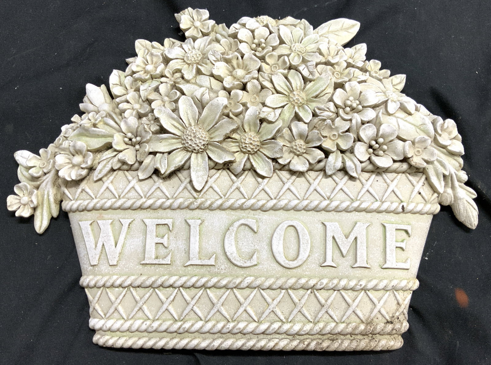 Cement Outdoor Welcome Wall Sign: Sign appears to be cement possibly composite. Sign reads WELCOME. Depicts an arrangement of flowers in a basket. Piece is white toned. Sign measures approximately 12 inches wide 9 inches tall. Welcome