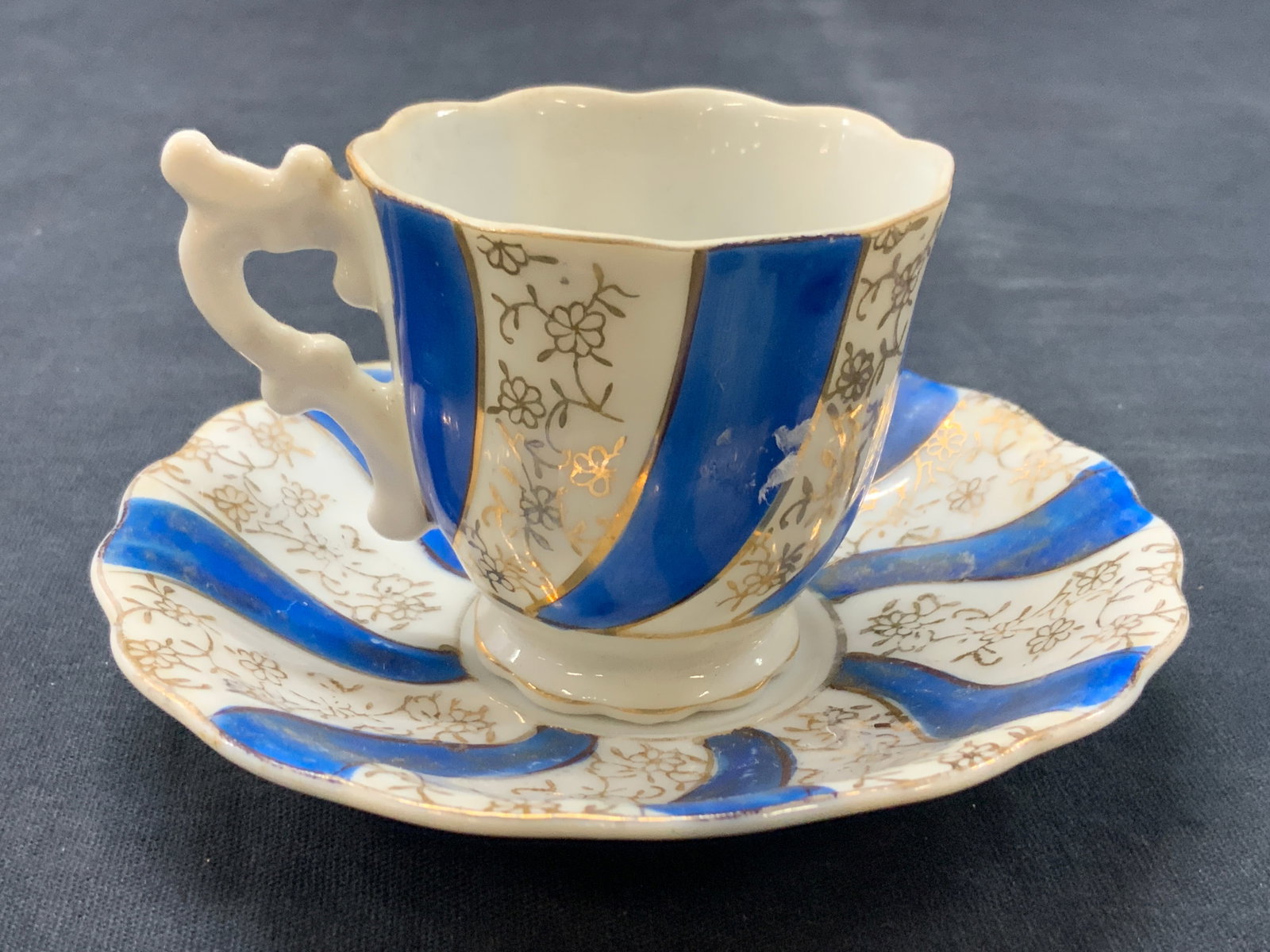 Hand Painted Porcelain Cup & Saucer, Japan: Hand painted porcelain cup and saucer with hand painted blue bands and girl floral motifs. Marked Japan on underside. Saucer measures 4 inch diameter and cup measures 2 inches tall and 2.15 inch diame