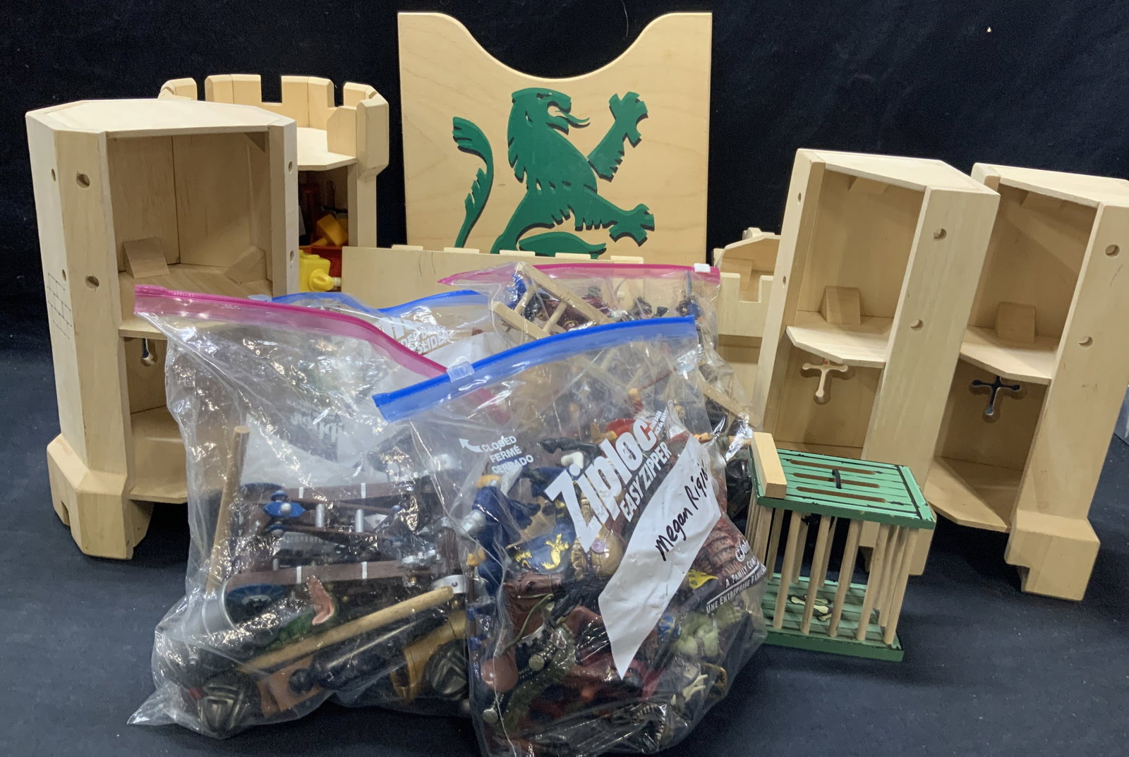 Ryans Room Wooden Toy Castle & More: Lot of 10+ Pieces. 1 wooden toy castle with put apart sections, marked Ryans room. 1 wooden shield with a green lion motif and various toy knights and action figures. Largest piece is 15 x 11 inches. 