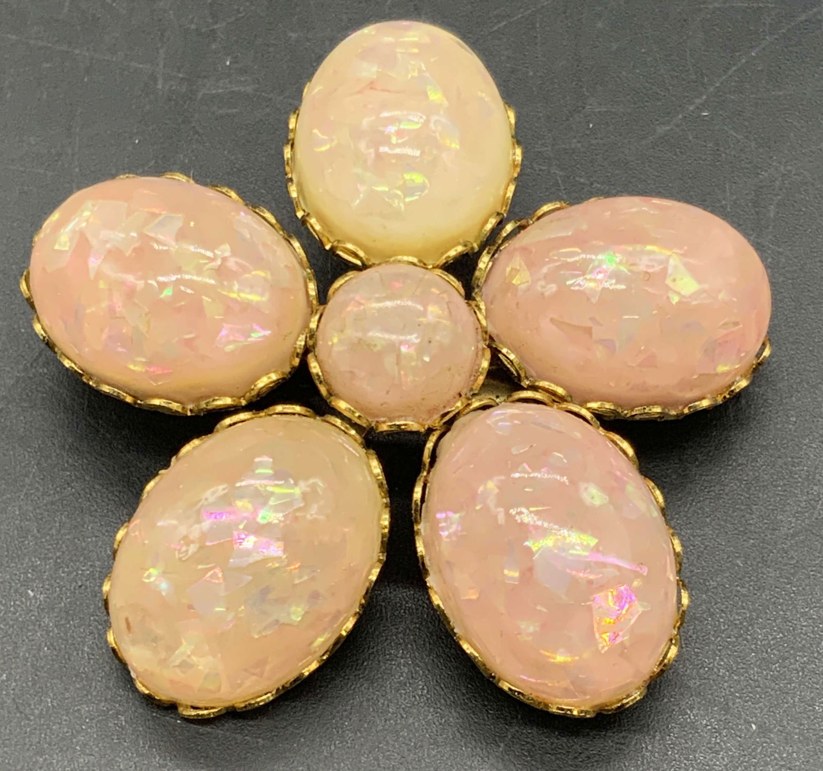 CORO Vintage Pink Shimmery Cabochon Brooch: A vintage gold tone metal floral form brooch bedecked with prong set shimmery pink hued costume cabochons. Reverse has a metal pin closure and is marked CORO. Measures approx. 1.75L x 1.75W in. Some s