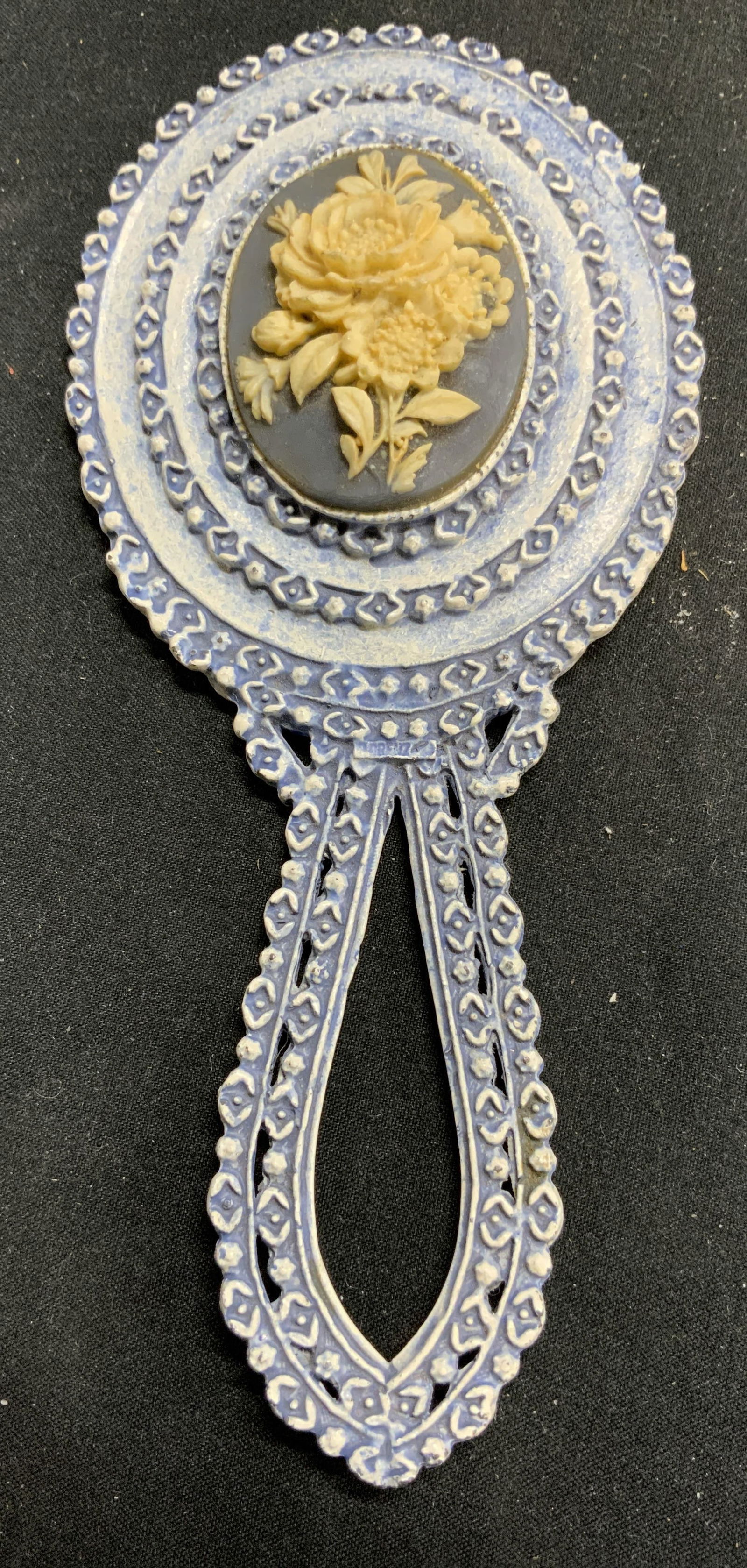 FLORENZA Vintage Resinous Hand Mirror: Mirror inscribed FLORENZA. Mirror is vintage. Piece is crafted from a resinous material. Mirror has oval shaped mirrored surface. Piece has handle. Backside is light blue toned with yellow toned flora
