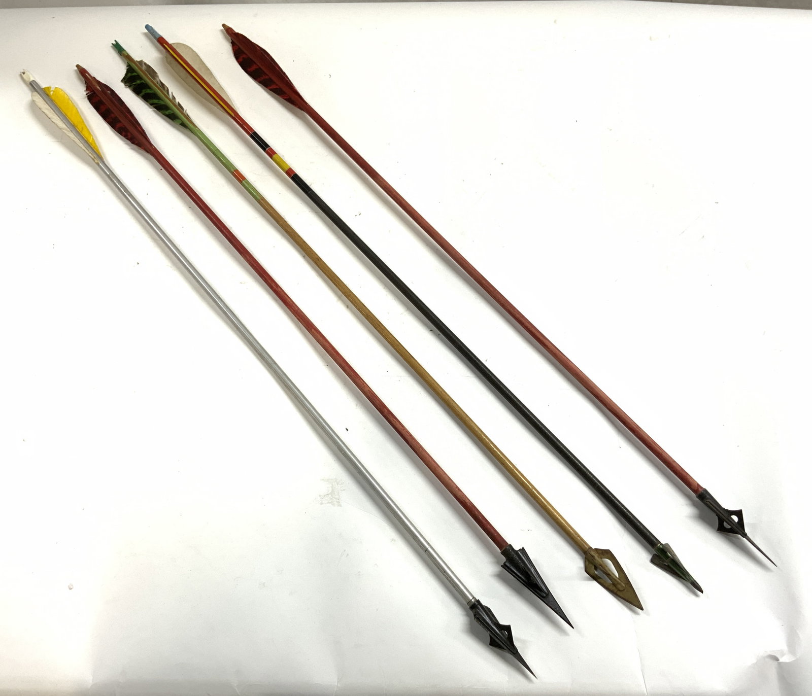 Lot 5 Assorted Archery Arrows: Lot includes 5 arrows. 4 appear to be wooden, 1 is metal. Arrow tips appear to be metal. Tails appear to be synthetic feathers. Largest arrow measures approximately 31.5 inches long. Arrows, wood arro