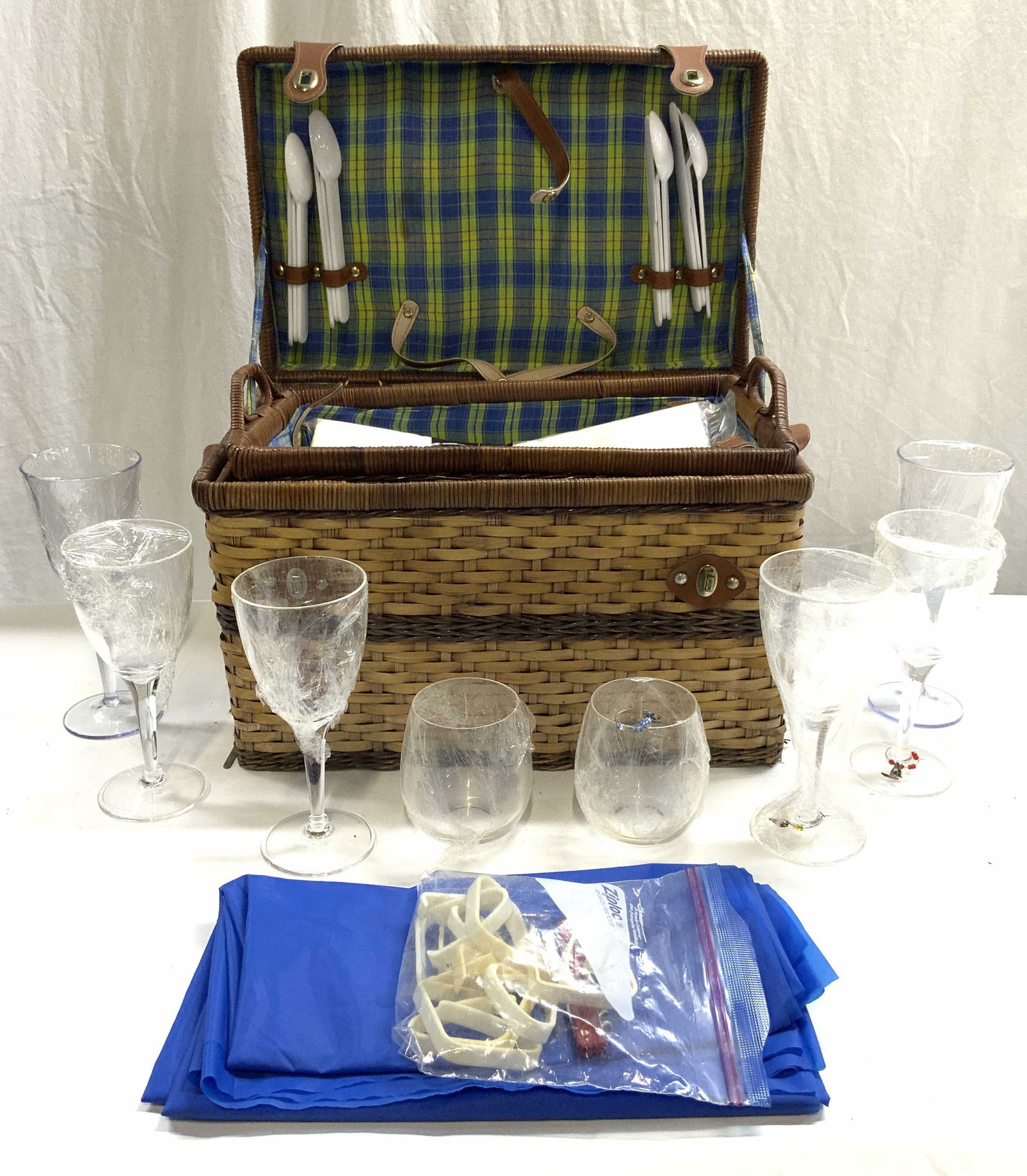 Set 10+ Woven Picnic Basket & Dining Accessories: Lot includes woven wicker picnic basket. Plastic cutlery, plastic goblets, 1 white and 1 blue table covering, 1 bottle opener, 1 wine corkscrew, & 1 tray. Basket has light brown toned leather areas. P