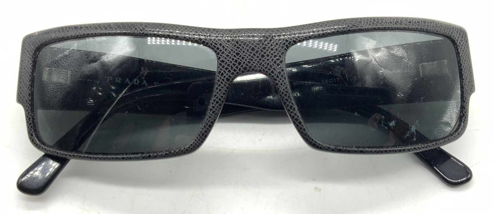 Prada Leather Style Sunglasses, Italy: Black toned leather patterned sunglasses, marked Prada on side and on arm of glasses. Made in Italy. Approx 5 inches wide and arms being 6 inches long. Moderate surface wearing to glasses and frame du