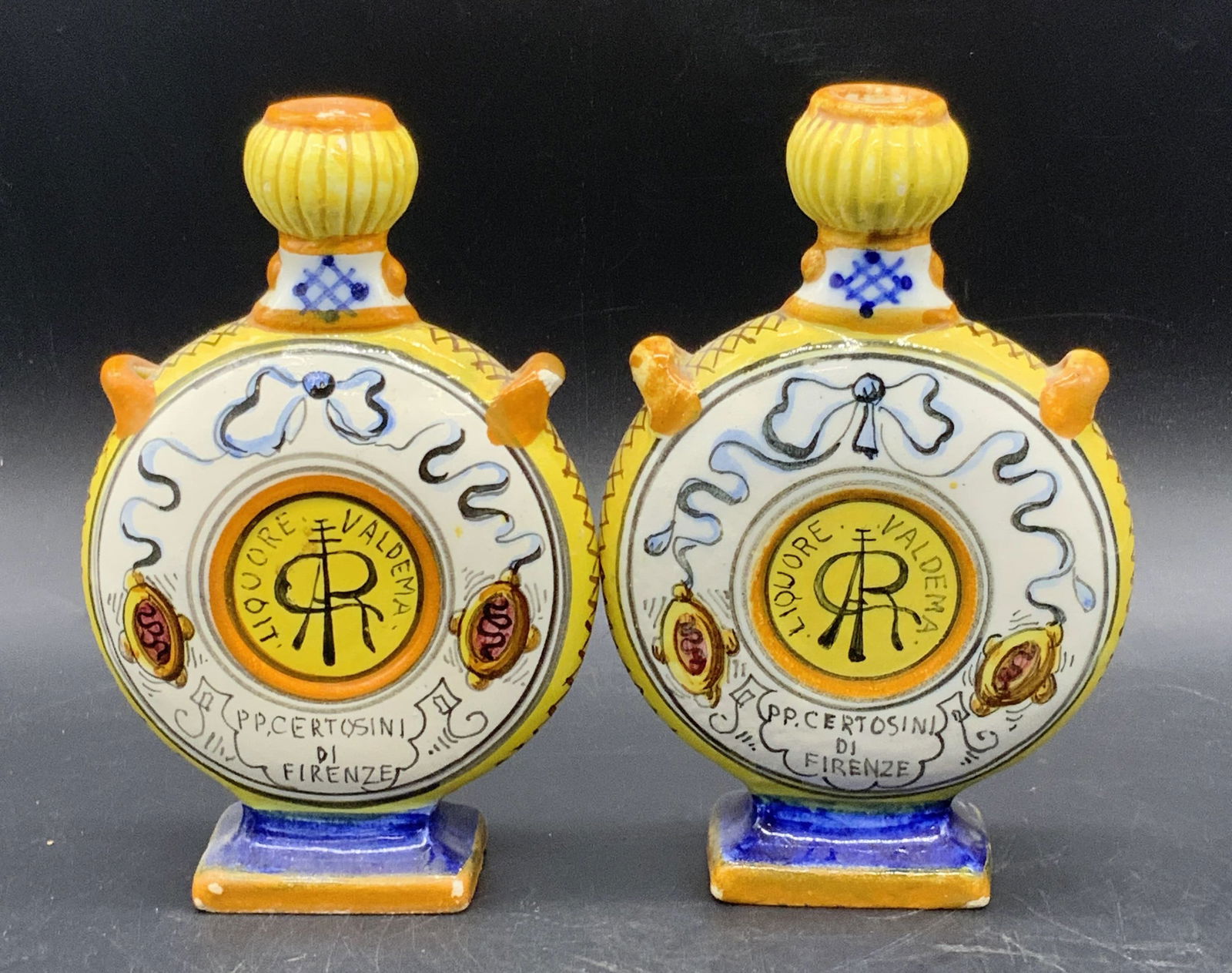2 Liquore Valdema Handmade Italian Pottery Bottles: A pair of vintage Liquore Valdema handmade and hand painted Italian pottery flasks / bottles / vessels. Serpentine, floral, ribbon, and geometric motifs throughout. Undersides read ITALY, and are trad
