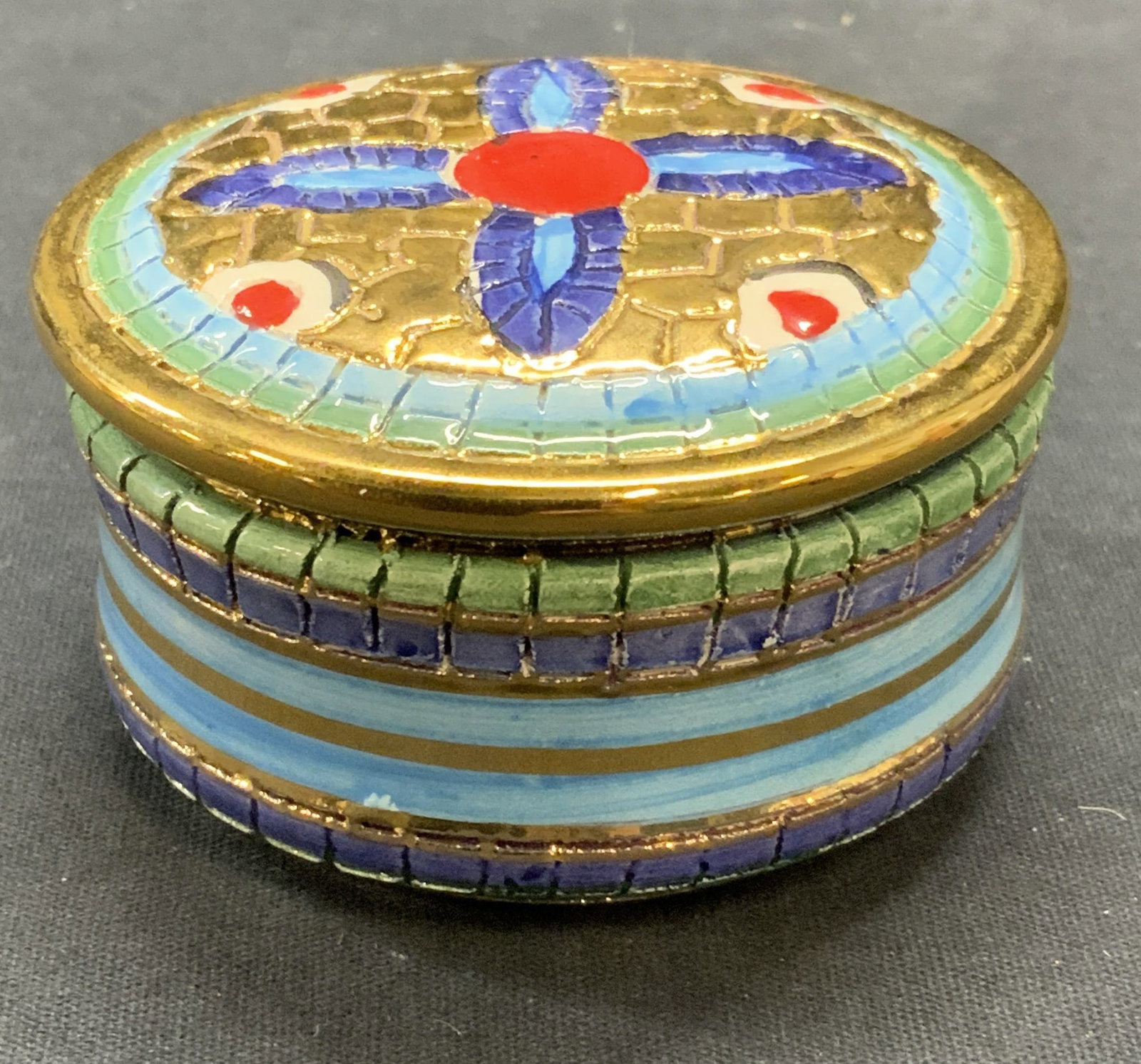 Assisi Gilt Porcelain Trinket Box, Italy: Assisi got porcelain trinket box. Etched surface with mosaic motif. Hand painted in hues of red and blue, signed to underside. Made in Italy. Measures approx. 3 x 1.5 inches. Some surface wear includi