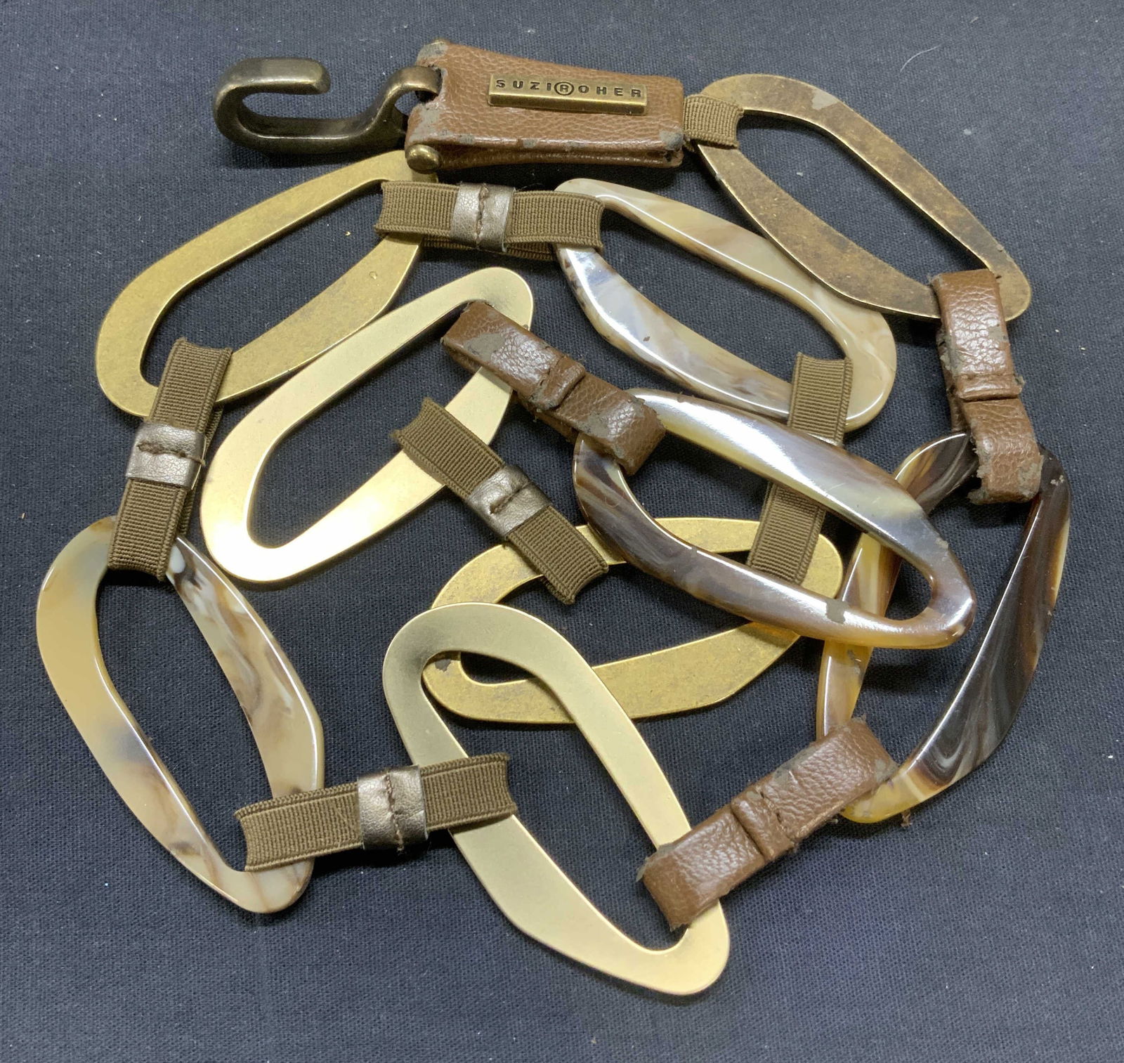 SUZI ROHER Gold Tn Brown Leather Belt: SUZI ROHER gold tone metal, marble lucite, and brown leather trim link belt. Signed on plaque. Measures approx. 35 inches long. Some scratching and losses to leather finish observed. SUZI ROHER, SUZI