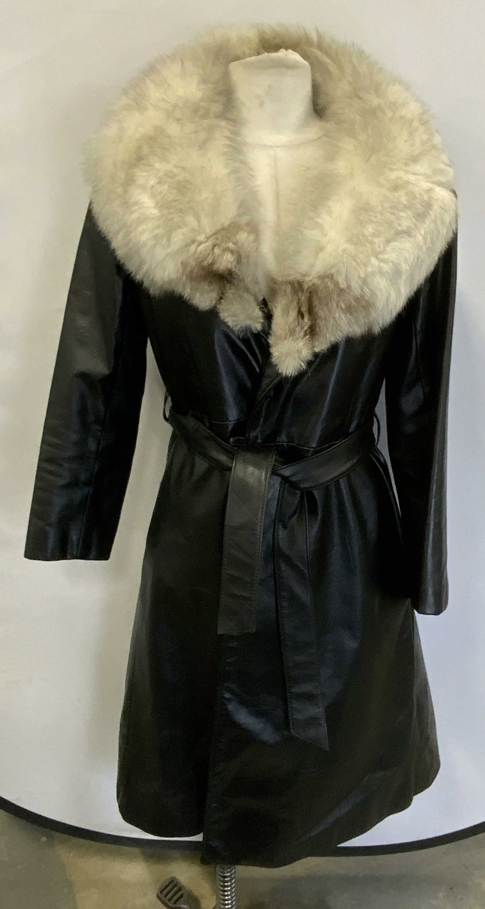 Black Leather Fur Trim Belted Trench Coat: Black leather belted trench coat with tan fur trim collar. Measures approx. 18 inches across chest and 41 inches from shoulder to hem. Some wear to material consistent with exposure including separati