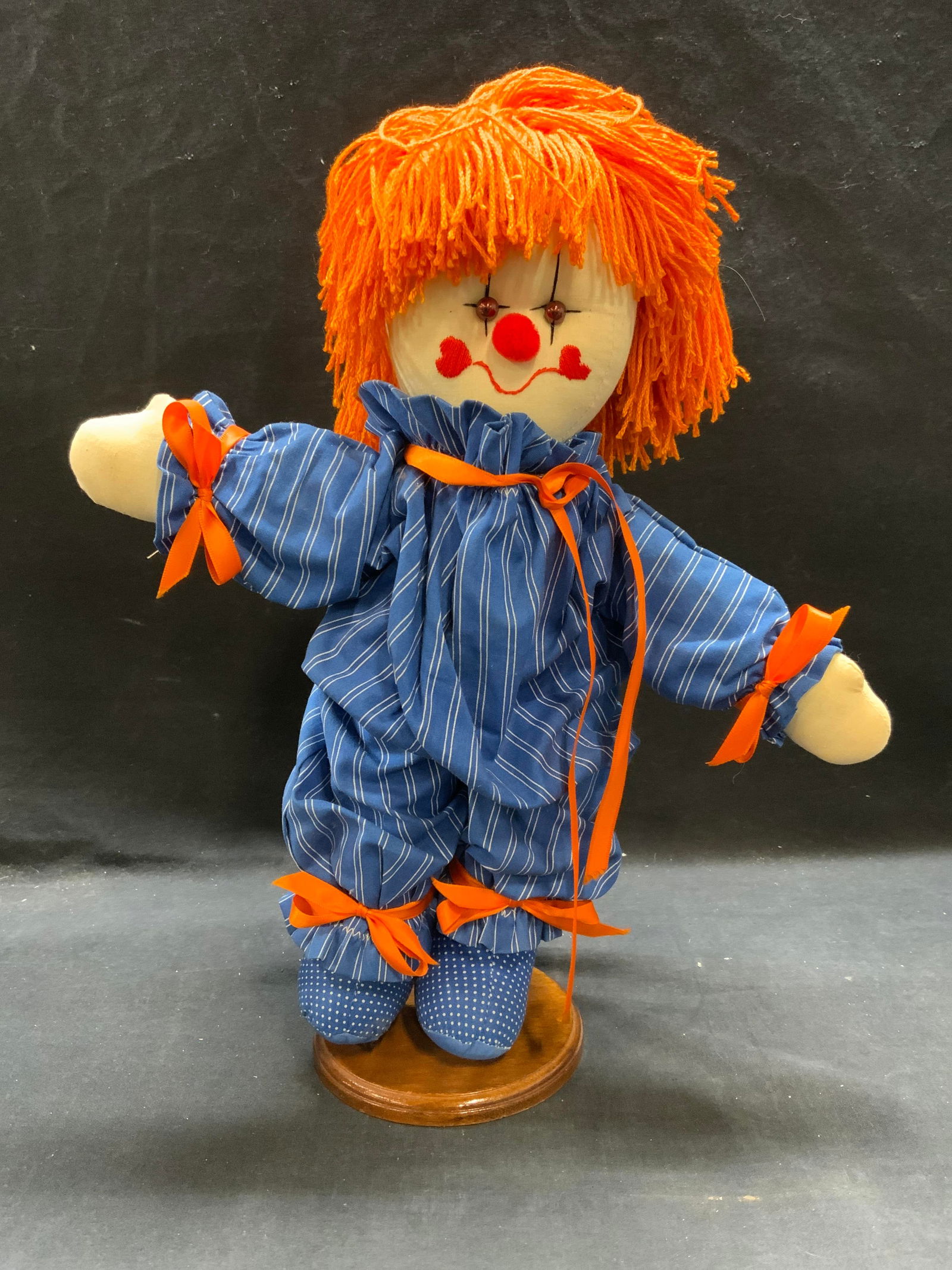 Clown Fabric Rag Doll13in: Fabric rag doll. Clown motif with blue jumpsuit and orange ribbon. Measures approx. 13 inches long. Includes doll stand. Some wear to material consistent with exposure. Clown, clown doll, doll, fabric