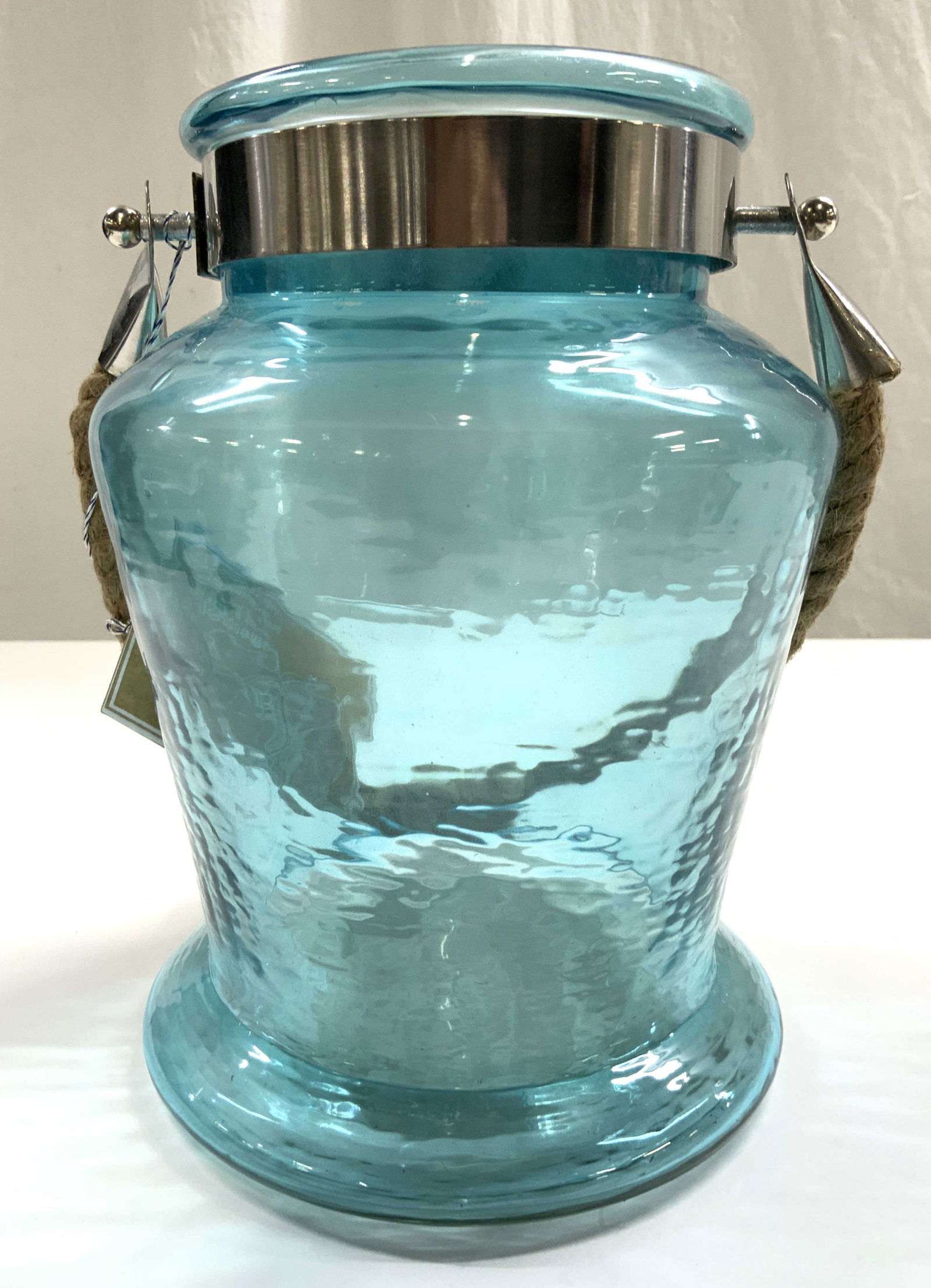 MARINA BY ACASIA Home Glass Jar W Handle Aqua: Tag reads MARINA BY ACASIA. Jar is aqua toned and glass. Piece has corded rope handle. Base of jar expands outward. Vessel measures approximately 9 inches tall 6.5 inches wide. Glass jar, Marina by Ac