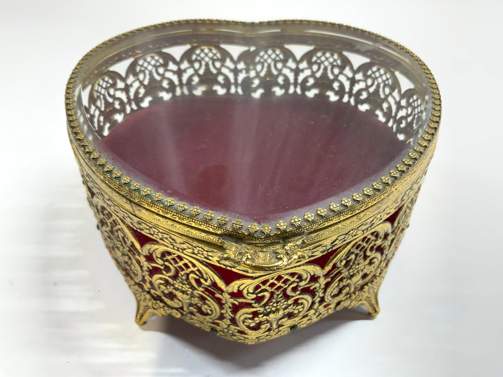 Vntg Gilt Metal Glass Top Heart Filigree Jewelry Box: Jewelry box is vintage. Piece is gilt metal, filigree with ornate scroll floral & leaf detail. Piece has hinged lid with beveled top. Interior and undersides are red toned crushed velvet. Piece has 4 