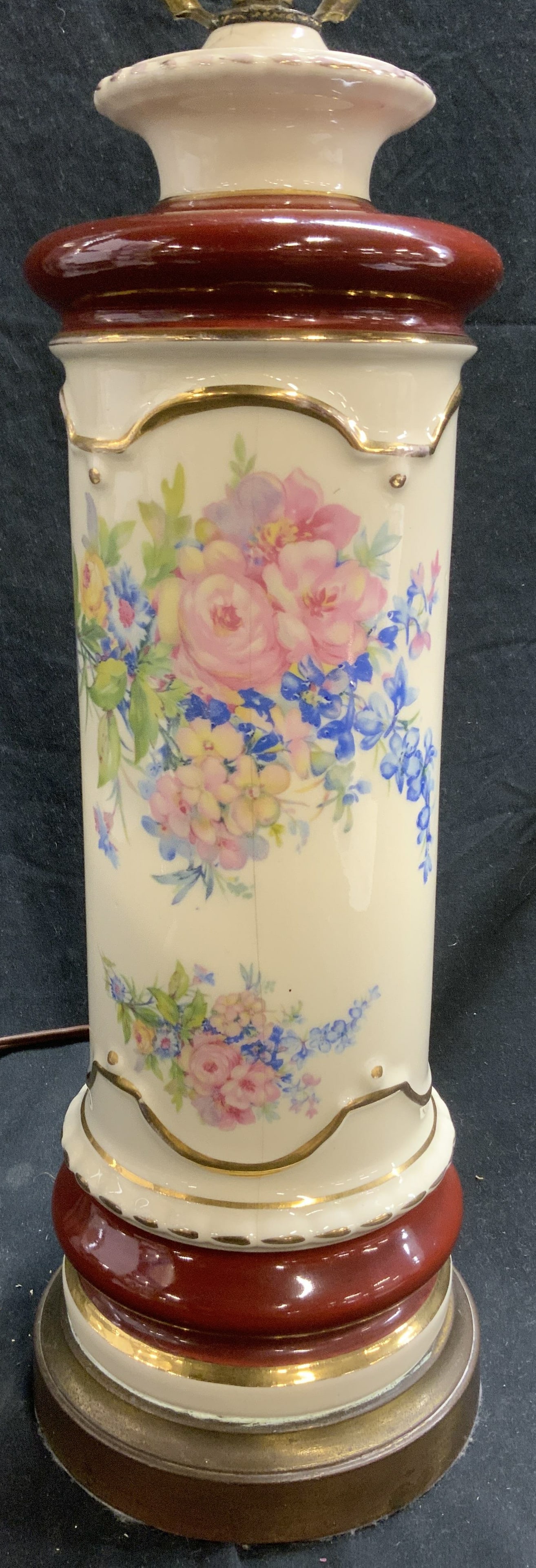 Vintage Porcelain Lamp W Floral Detail 26inH: Lamp is vintage and porcelain. Piece has multi toned floral and leaf detail. Lamp is cream and maroon toned with areas of gilt. Base is circular shaped and metal. Lamp includes harp and finial. Piece