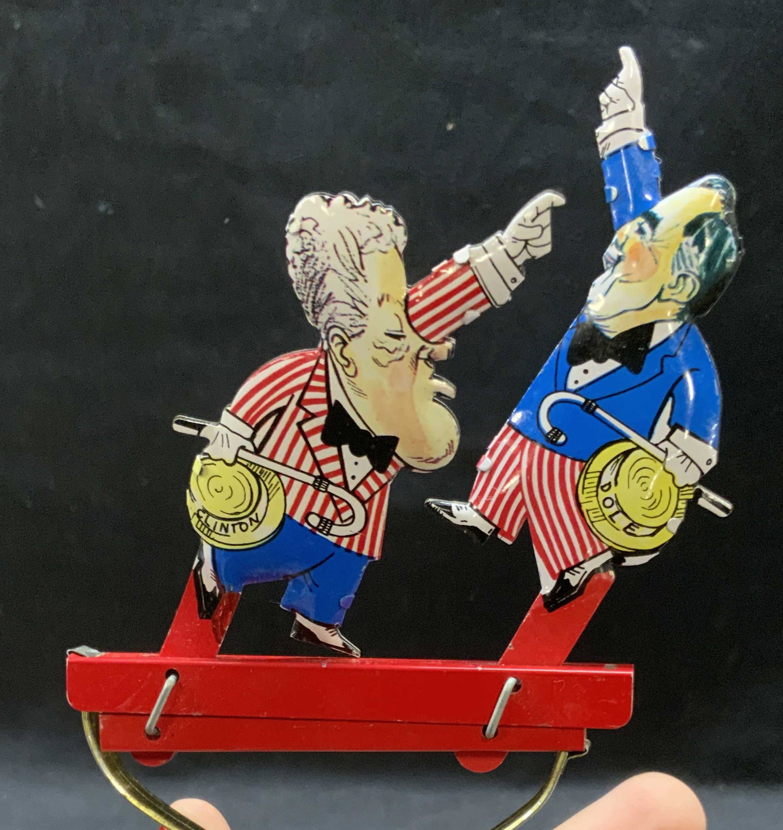 Vntg Bill Clinton & Bob Dole Great Debate Tin Toy: A vintage 1996 Bill Clinton and Bob Dole ‘ The Great Debate ‘ Tin Toy. Piece is articulated. Primarily red, white, and blue hues. Measures approx. 6.25L x 3.25W in. Some wear consistent with age, 