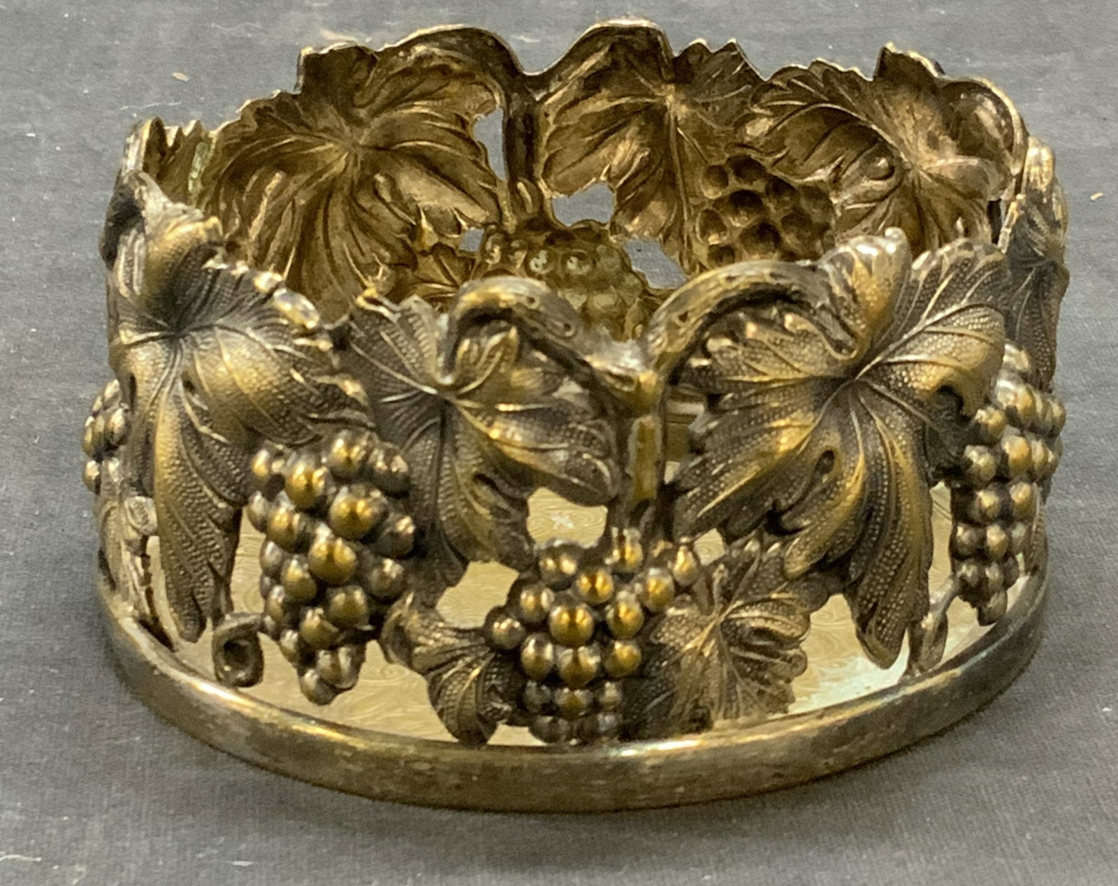 Topazio Silver Plated Wine Bottle Coaster: Topazio silver plated wine bottle coaster. Pierced raised grape vine motif. Trademarked to underside. Made in Portugal. Measures approx. 4 x 2 inches. Some surface wear including scratching and loss t