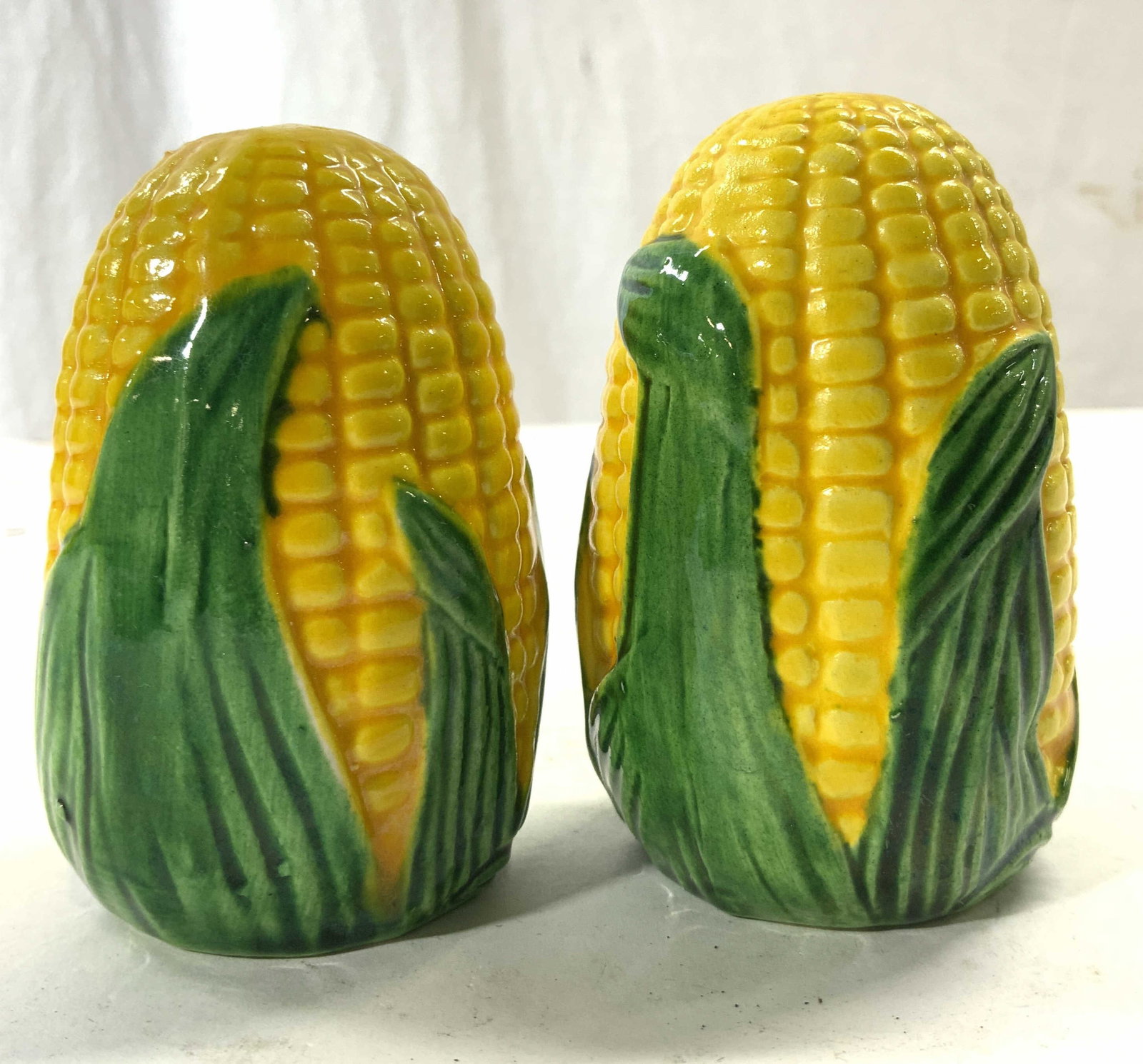 Pair Porcelain Corn Salt & Pepper Shakers: Lot includes 1 salt & 1 pepper shaker. Each piece is yellow and green toned. Shakers have ear of corn form. Each piece is porcelain. Each appear to be hand painted. Measures approx 3 1/4 in by 2 in. S