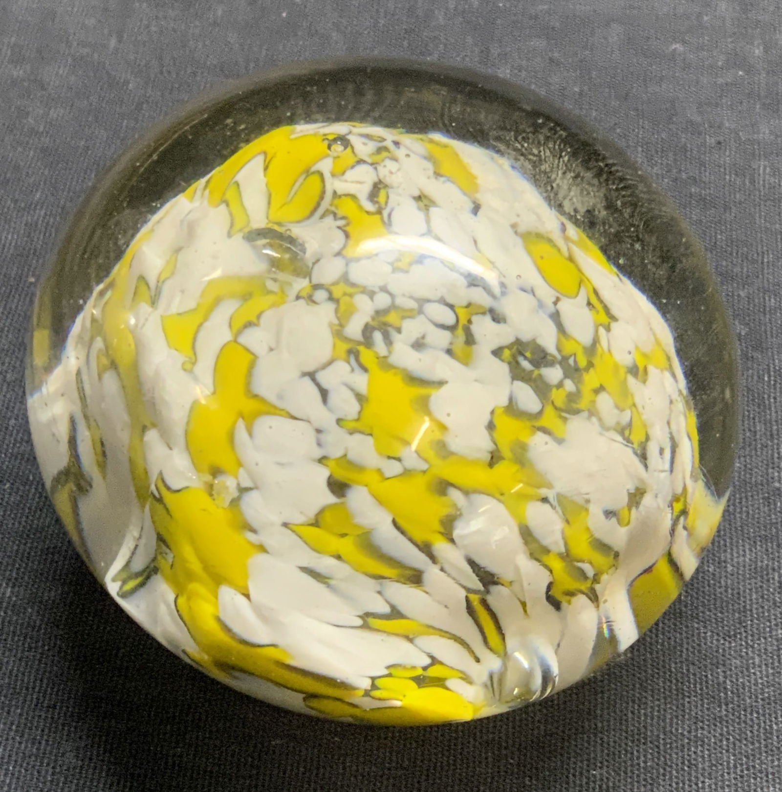 Art Glass Yellow & White Paperweight: A clear art glass paperweight accented by yellow and white hues. Measures approx. 2.25H x 2.25W in. Some bubbles to interior. Some surface wear present. Collectibles, art glass paperweight, desktop ac