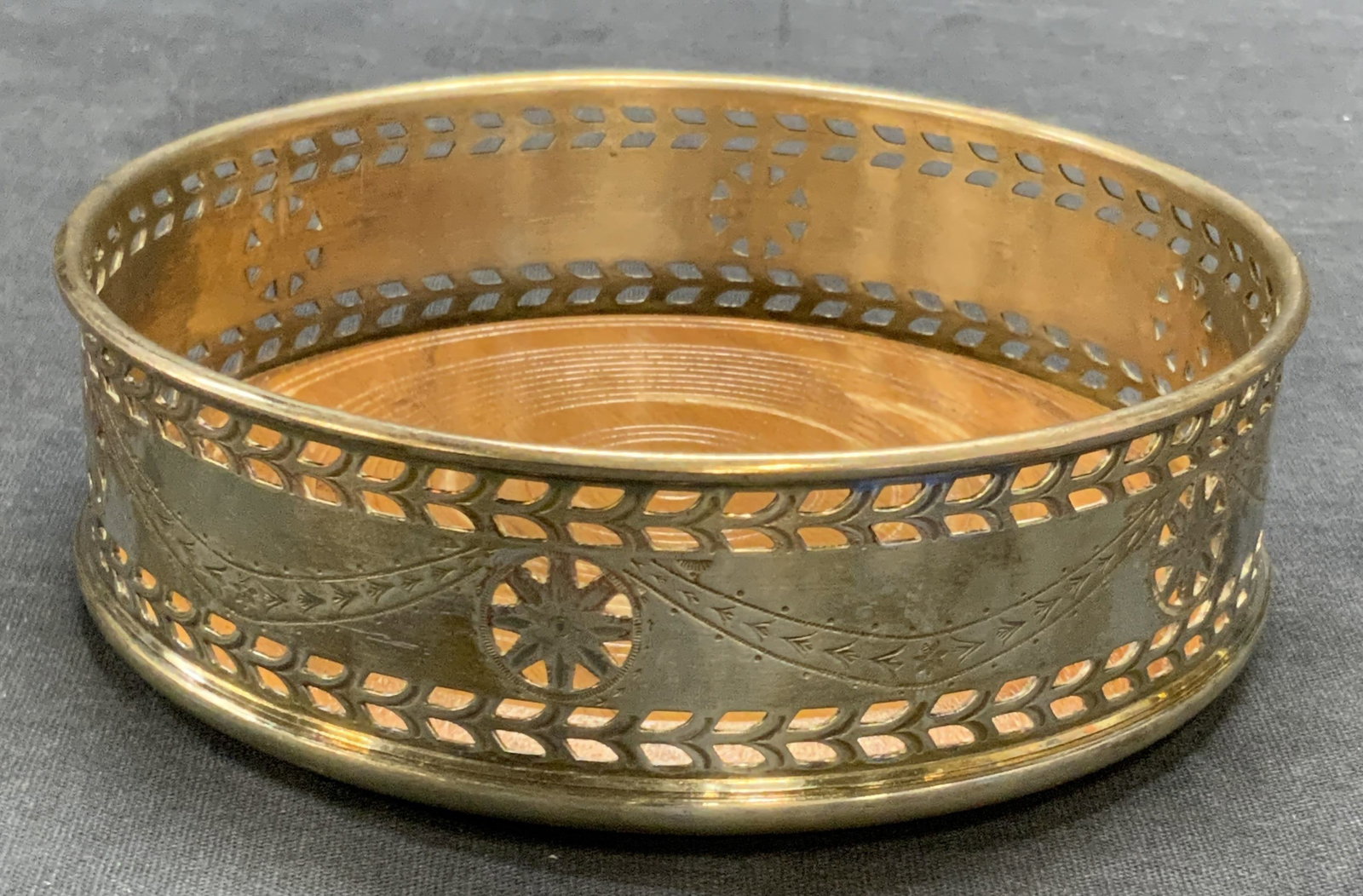 KIRK STEIFF Silver Plated Wooden Wine Coaster: A silver plated wooden wine bottle coaster. Pierced metalwork along the sides. Signed KIRK STEIFF SILVERPLATE to rim interior. Measures approx. 1.5H x 5W in. Green felt to underside. Discoloration and