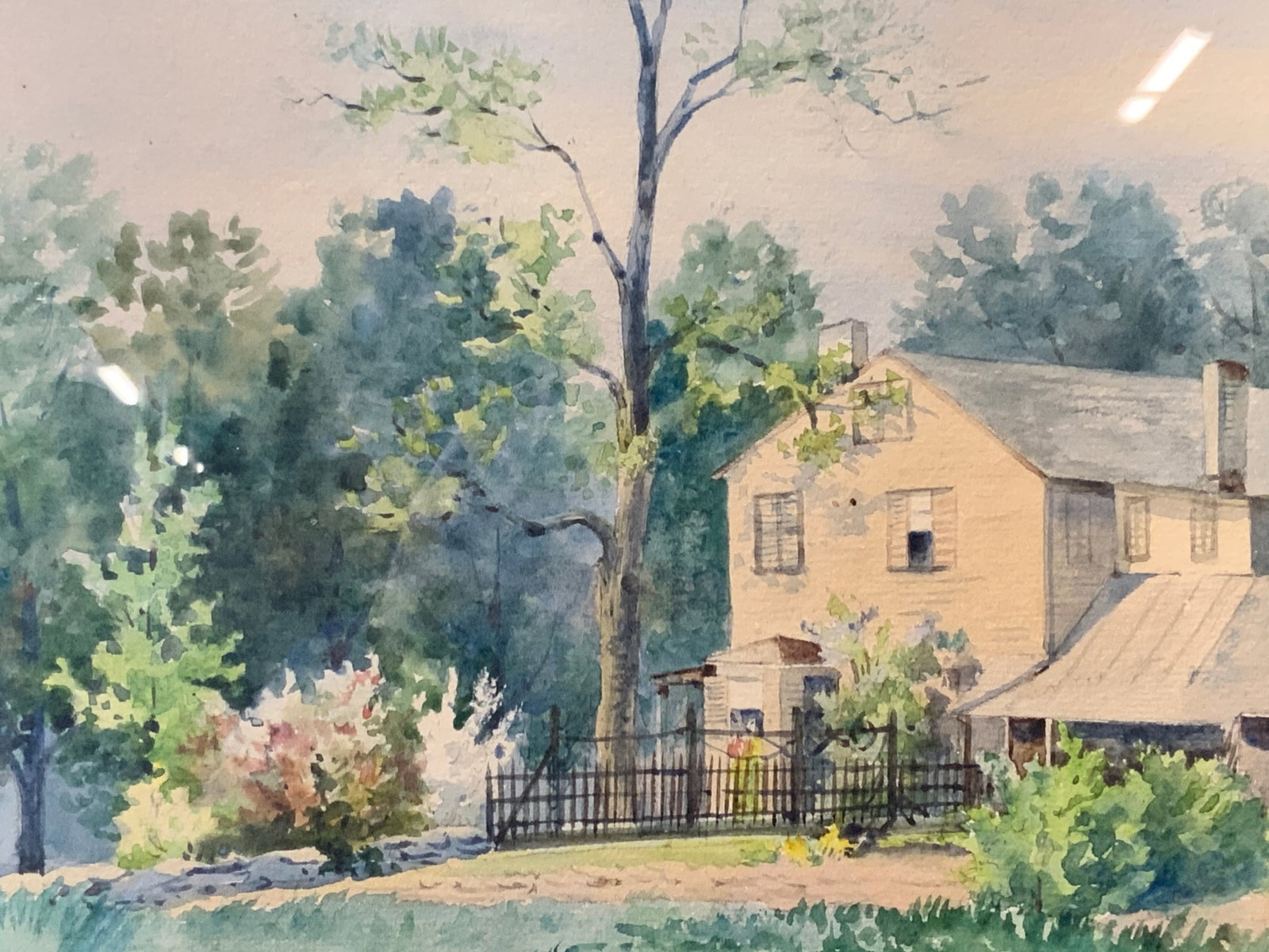Summer Home Watercolor: Subject depicts a view of a white home surrounded by bushes and trees. Framed in a wooden frame. Frame measures approx. 18.5W x 14.75H in. Window measures approx 13.5W x 9.25H in. Not viewed outside o