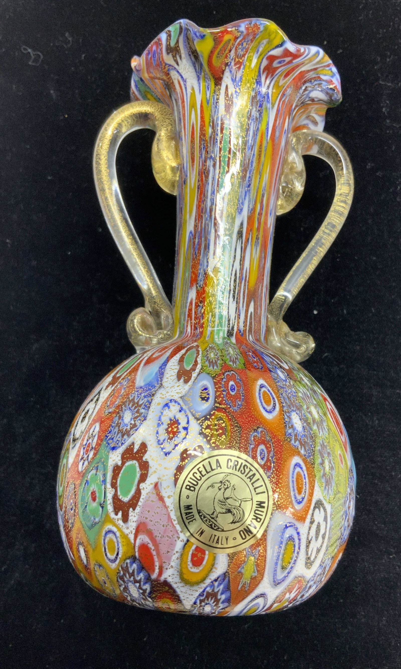 BUCELLA CRISTALLI MURANO GLASS VASE, Italy: BUCELLA CRISTALLI millefiori MURANO Art glass vase with 24 k gold flecks and textured exterior. Sticker label on vase reads BUCELLA CRISTALLI MURANO MADE IN ITALY. Furled rim with clear glass handles.