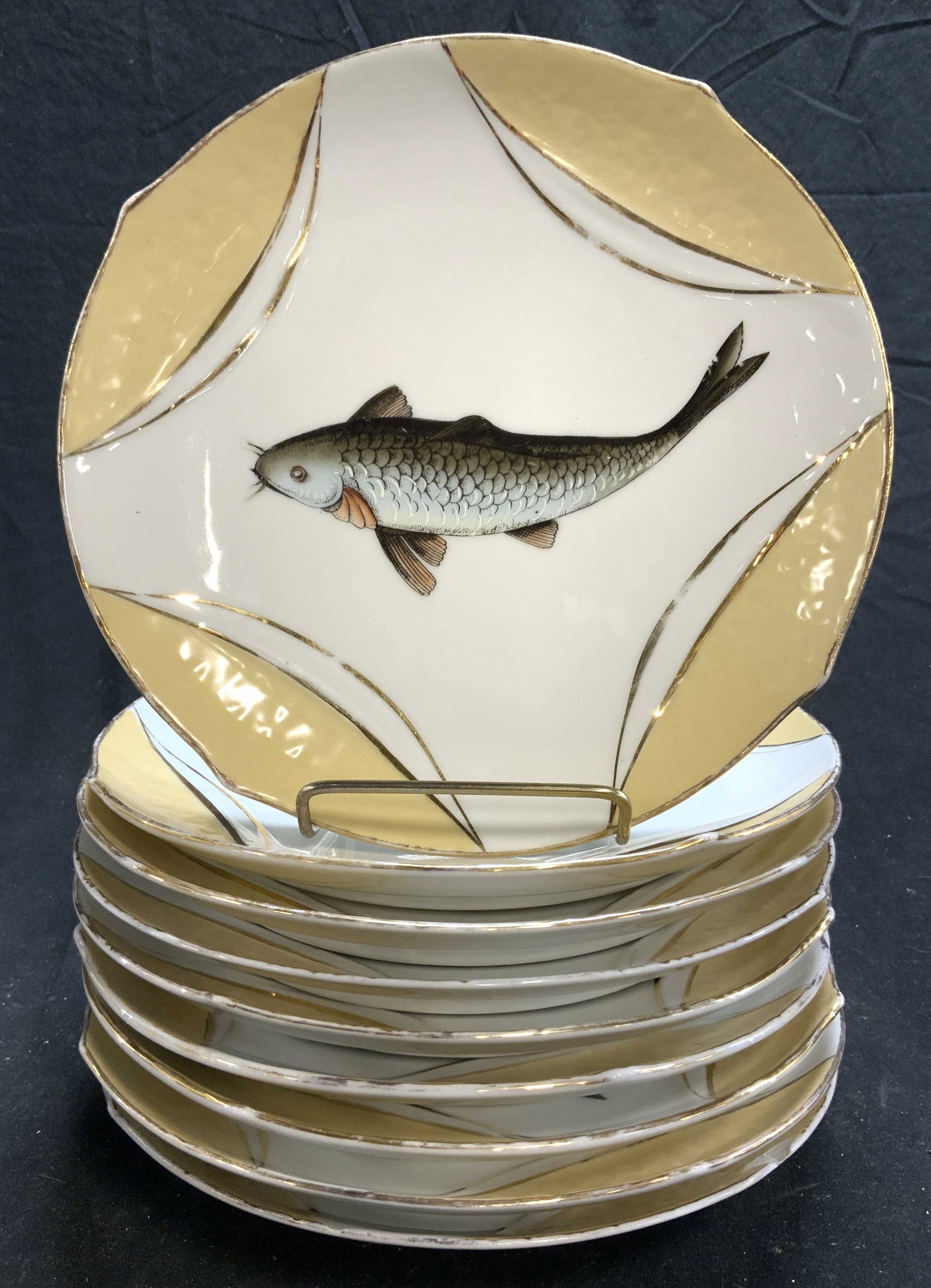 KARLSBAD H&CO Set 9 Porcelain Plates: Undersides of each plate are marked KARLSBAD H&CO. Lot includes 9 plates. Each are porcelain, white and cream toned with gilt areas & fish detail. Each plate measures approximately 8.5 inches diameter