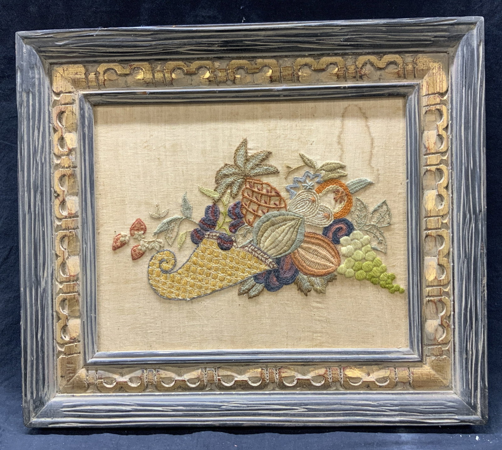 Framed Cornucopia Harvest Embroidery: Embroidery on cloth. Subject depicts a cornucopia with different fruits spilling out. Framed in ornate gilt wooden frame. Frame measures approx. 19 H x 22 W in. Window measures approx. 12 H x 15 W in.