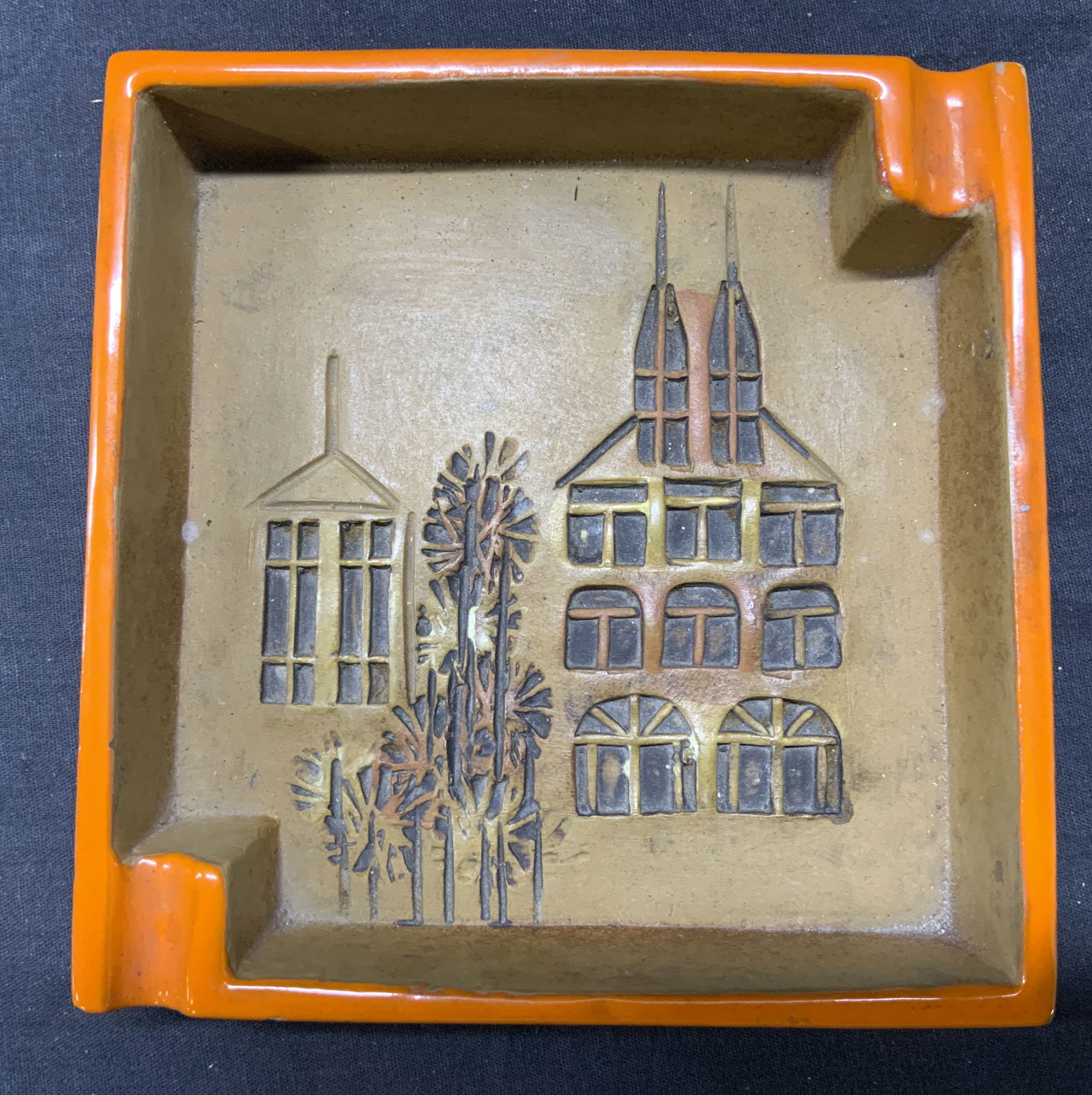 ALDO LONDI BITOSSI POTTERY Campus Line Tray Italy: Underside is marked for ITALY. Ash tray is ceramic. Piece has orange toned exterior. Interior is tan toned with relief architectural detail depicting 2 buildings and trees. Piece has 2 rests at corner