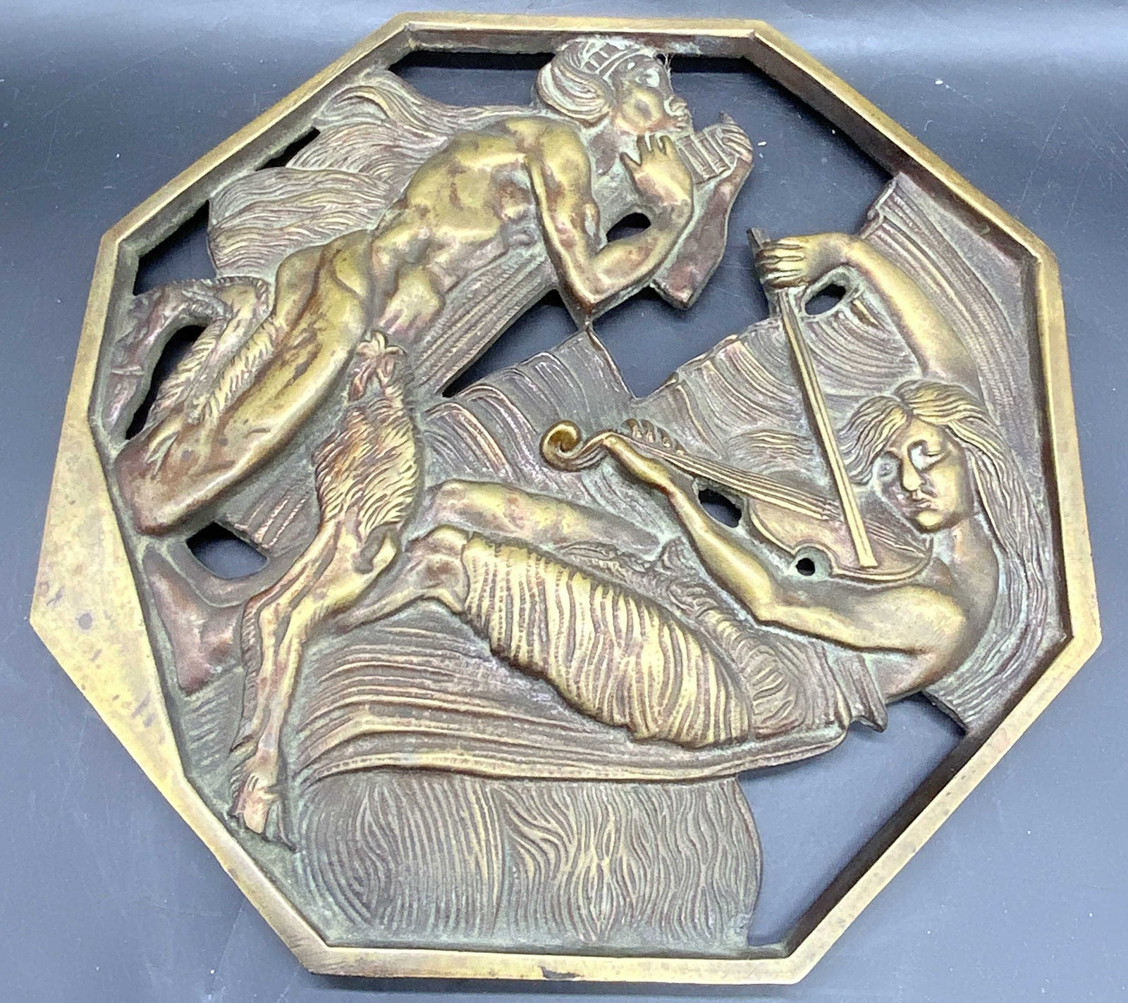 E.S Signed Vntg Satyr & Violinist Sculptural Plaque: A vintage Sculptural Plaque depicting a Satyr & Violinist in an Octagonal Frame. The plaque portrays a satyr with goat legs and a female violinist. Reverse is signed E.S. Crafted from gilded metal, po