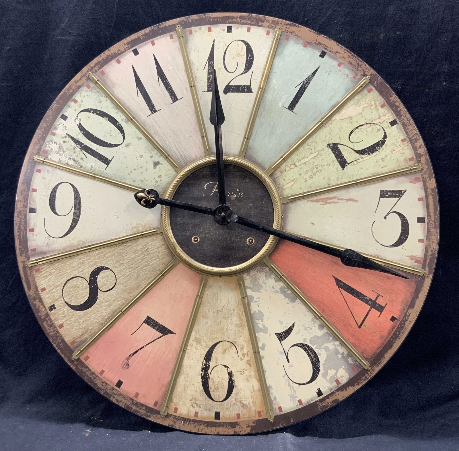 XL Multicolored Wooden Farmhouse Wall Clock 29i: Printed on wood. Metallic bindings affixed to clock face with nails. Center reads Paris. Clock measures approx. 29 W x 29 H in. Battery operated, requires 1 AA battery. Batteries not included. Not vie