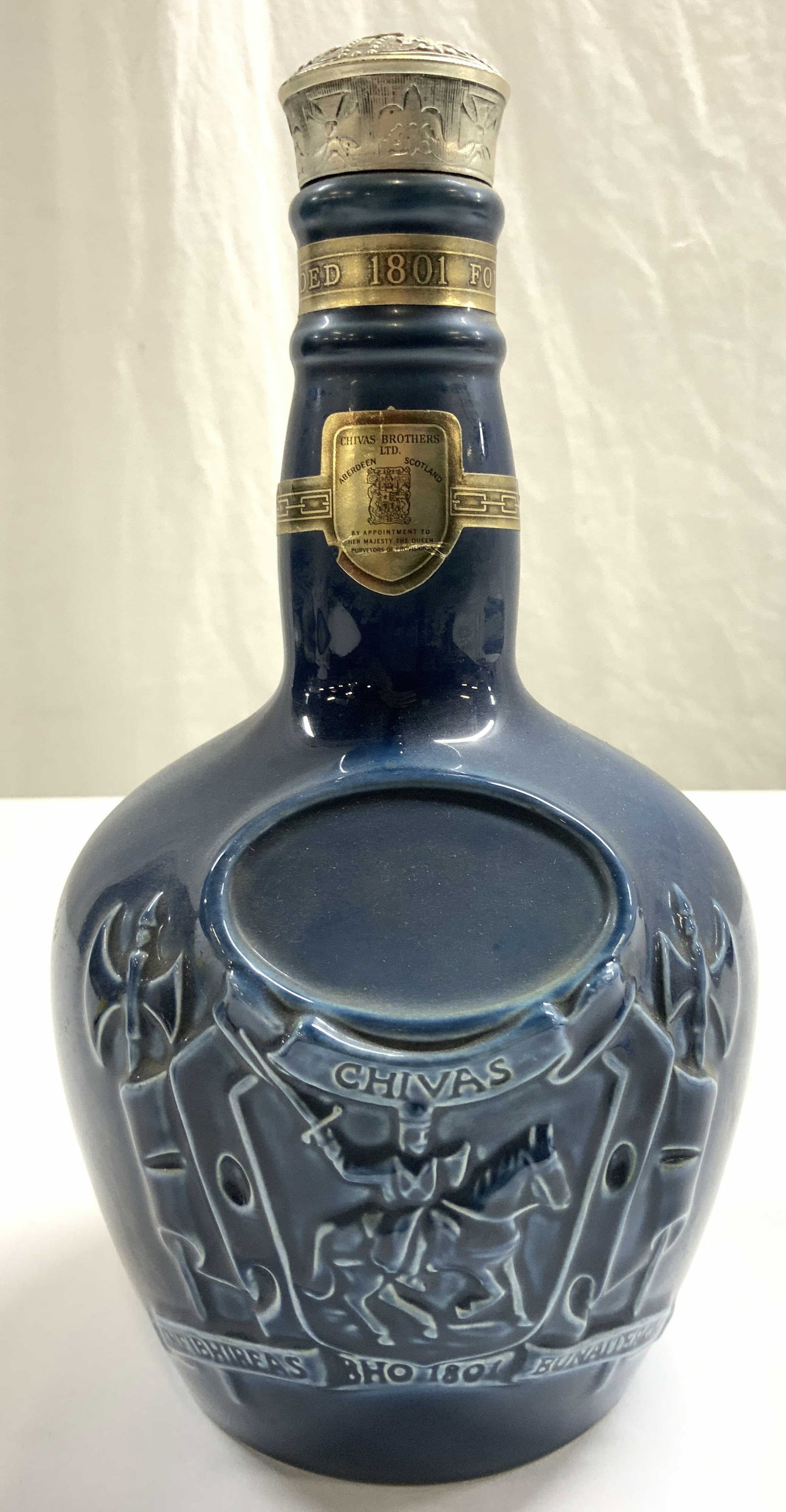 CHIVAS BROS Ceramic Scotch Bottle W Cap: Label reads CHIVAS BROS ABERDEEN SCOTLAND. Bottle is blue toned, appear to be ceramic. Piece has silver toned cap. Bottle has beveled derail depicting knight in armor riding horseback. Piece measures 