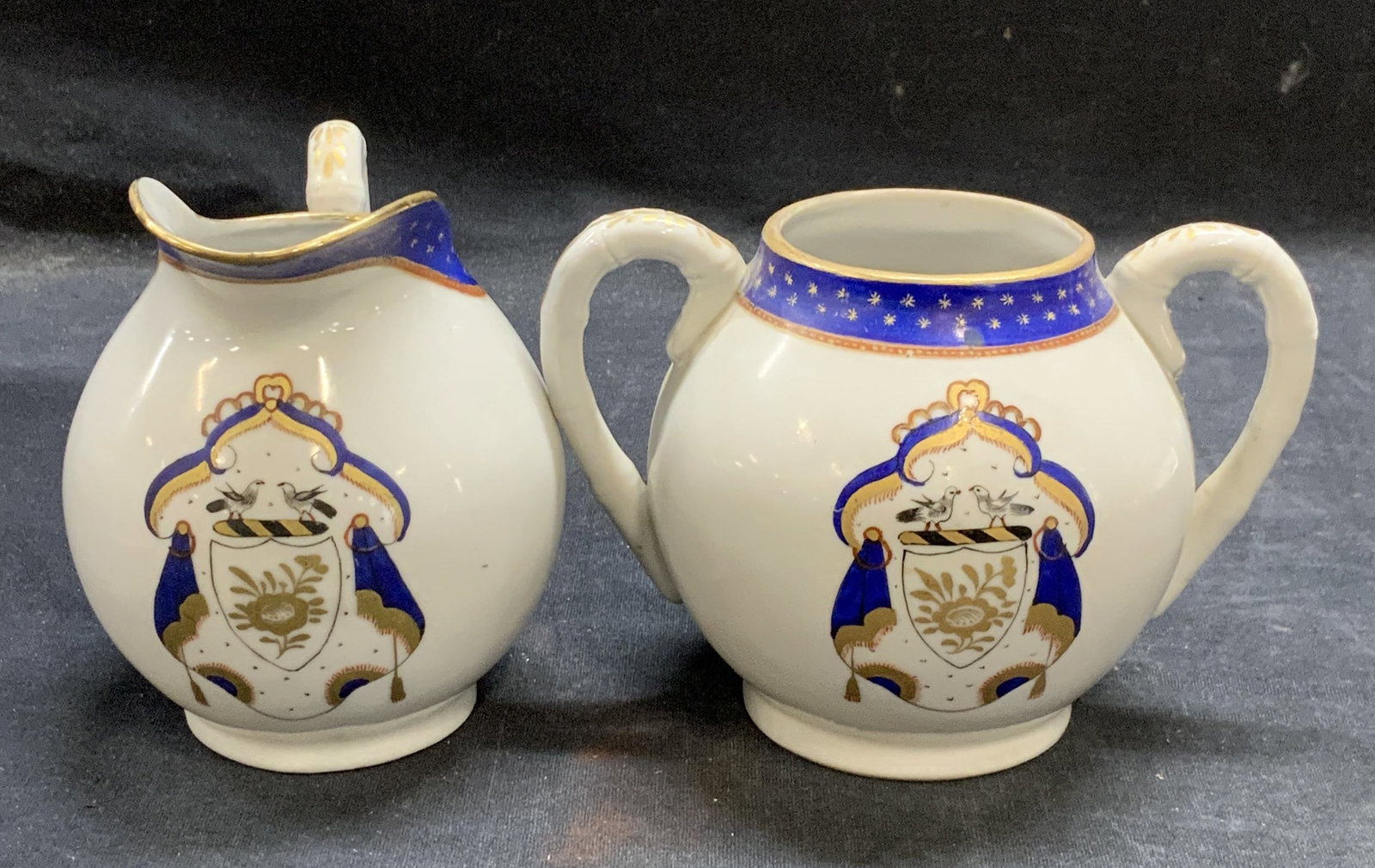 Vntg Hand Painted Porcelain Sugar Bowl & Creamer: Vintage hand painted porcelain sugar bowl and creamer with crest motif in blue and white with gilt decoration. Marked hand decorated in Hong Kong. Sugar bowl measures approx. 5.5 x 3.5 x 4 inches. Cre