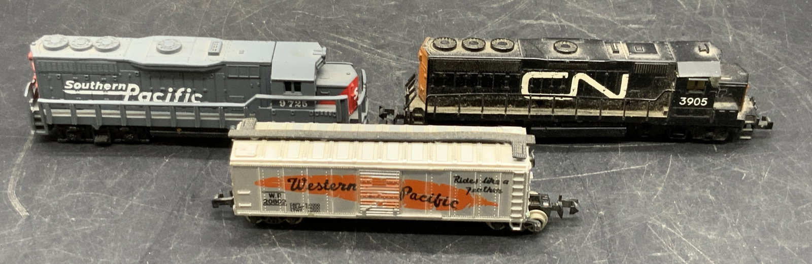 Lot 3 Train Toys, Yugoslavia & More: Three train toys. Pieces are crafted from composite materials. Sides are marked WESTERN PACIFIC, SOUTHERN PACIFIC, and CN. One marked YUGOSLAVIA to the underside. Largest piece measures approx. 1H x 4
