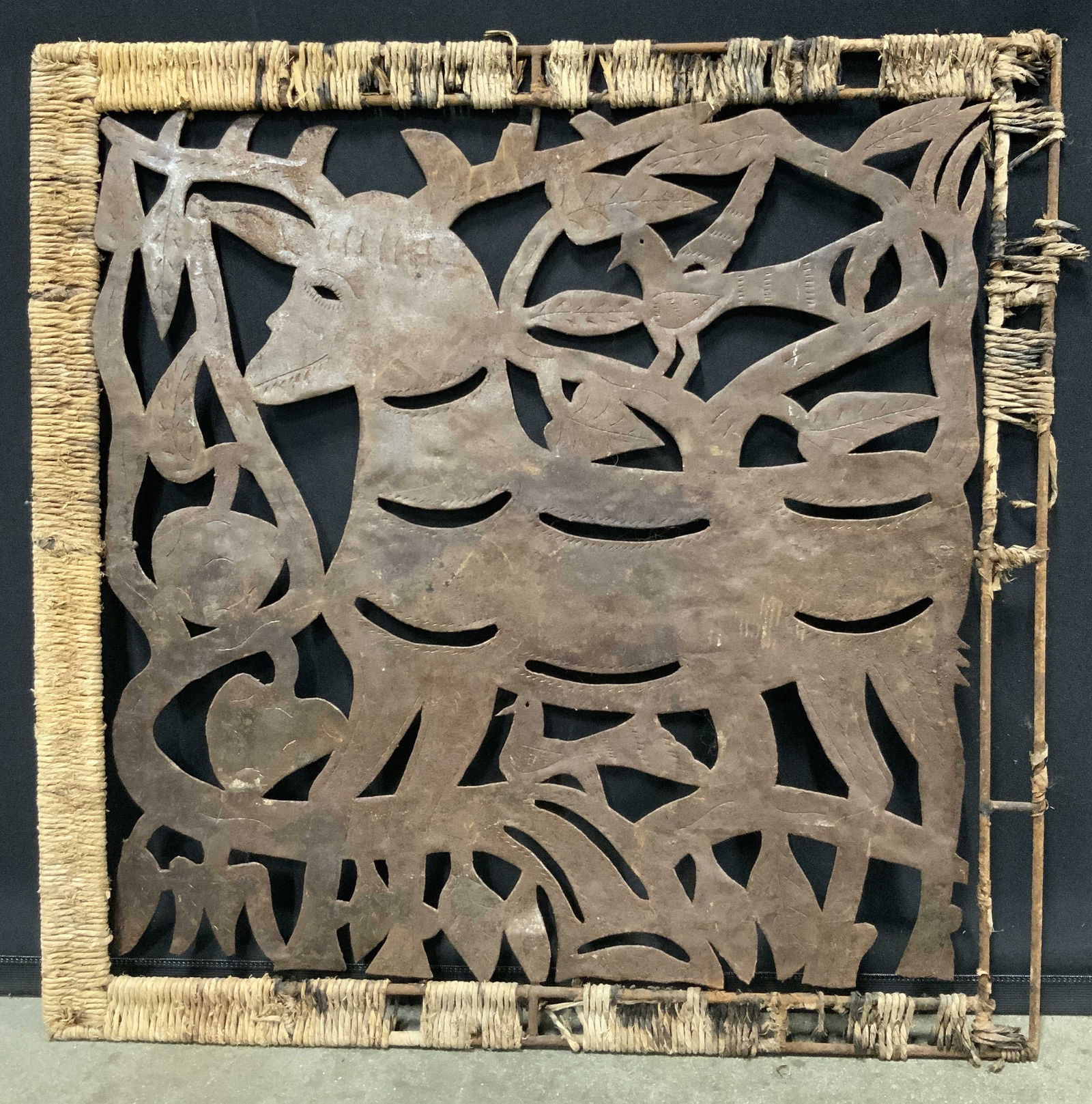 2D Carved Metal Art Deer With Birds 25in: Wrought iron metal with twine frame. Subject depicts a 2D carving of a deer with two birds and foliage. Framed in wrought iron frame wrapped in twine. Frame measures approx. 25 W x 25 H in. Losses in