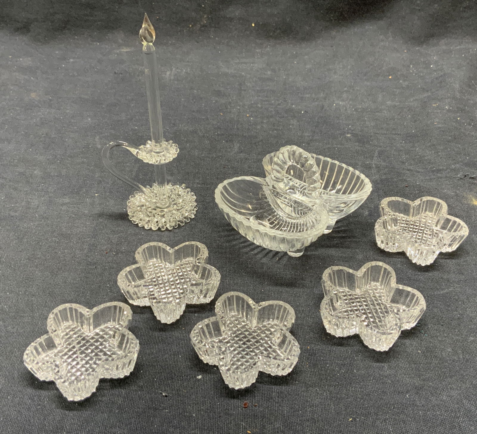 Lot 7 Glass Candlestick & Salt Cellar: Lot includes 1 glass candlestick, 5 floral form salt cellars & 1 basket form salt cellar. Each piece is glass. Basket Salt cellar measures approximately 2.75 inches wide 2 inches tall 2.5 inches deep.