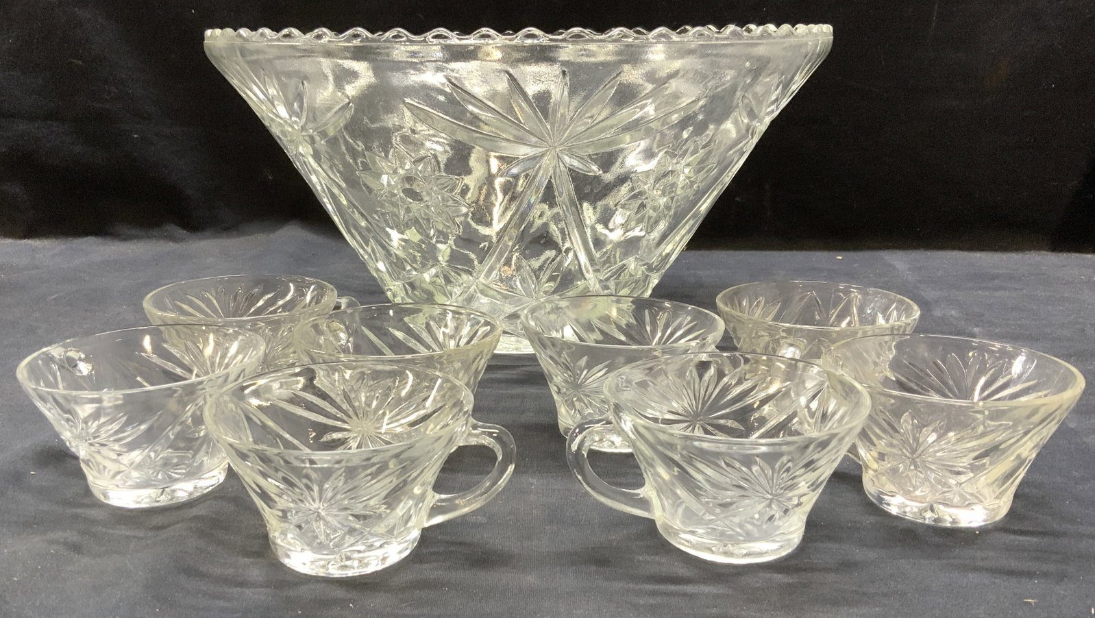 Set 9 Mid Century Cut Glass Punch Bowl: Heavy thick walled cut glass punch bowl with 8 matching cups. Bowl has a decorative rim. Hand cut glass with Star patterns. Punch bowl measures 7 in tall x approx 14 in. Wide. Cups measure 3.5 in. dia